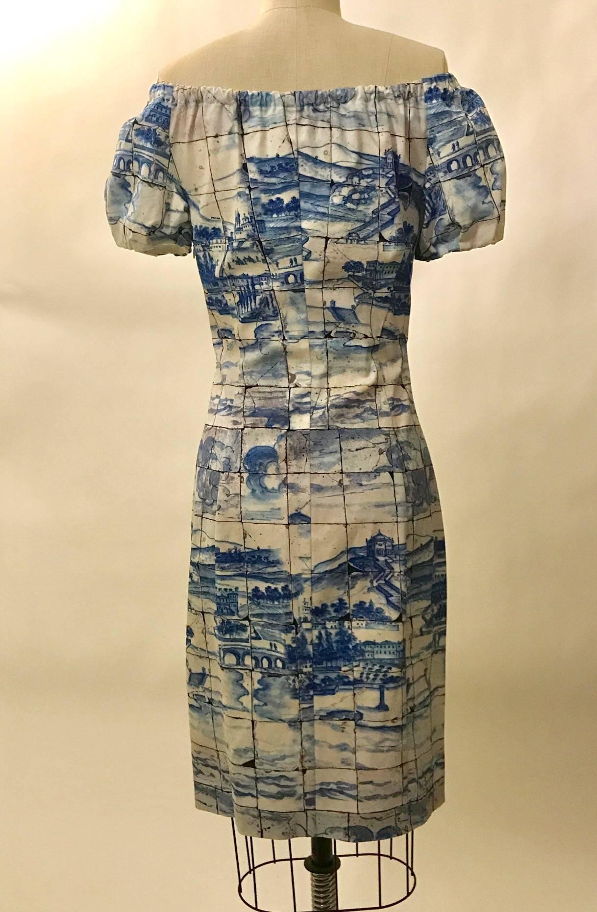 Prada blue and white scenic tile print dress from the Resort 2011 collection. Faint pink and earth colored watercolor tones scattered throughout. Elastic at neckline and sleeves allows it to be worn off the shoulder. Side zip.

97% cotton, 3% other.