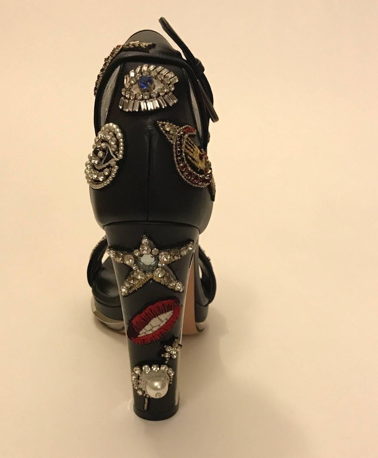 Alexander McQueen 'Obsession' sandal from Sarah Burton's Fall 2016 collection. Black lambskin leather with embroidered good luck charms and dream symbols accented with crystal rhinestones. Mirrored detail at heels and front. Ankle straps with