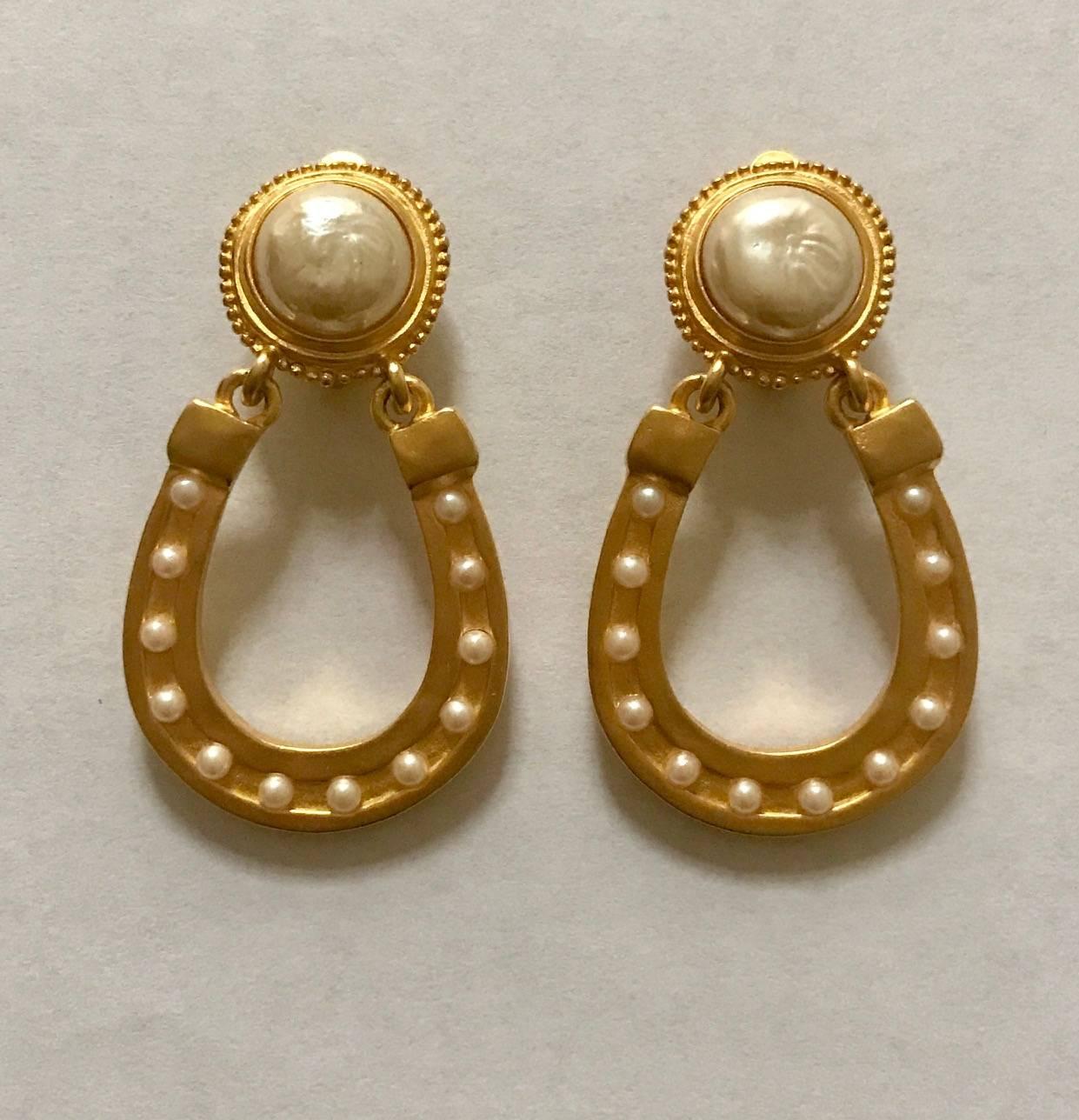 Karl Lagerfeld vintage satin finish gold tone clip on horseshoe earrings. Large faux pearl at top, and small faux pearls throughout horseshoe. Clip fastener.

Approximately 2.5