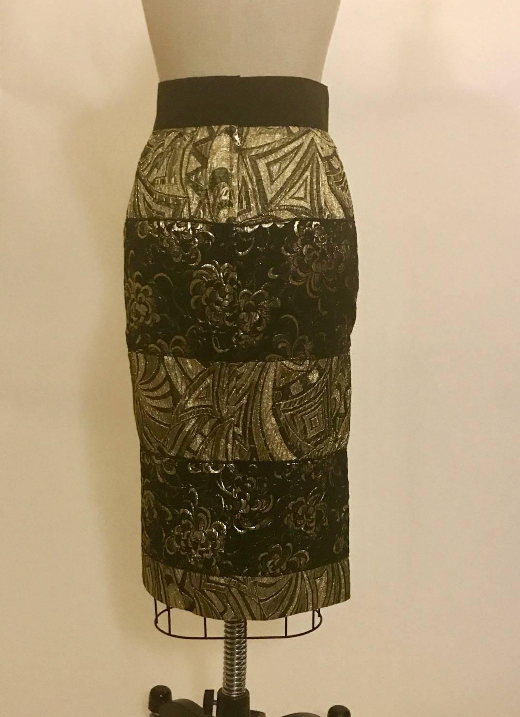 Dolce & Gabbana metallic gold and black jacquard skirt with alternating panels of floral and geometric patterns. Grosgrain waistband. Back slit at center. Closes at back with a zip and two snaps.

74% polyester, 19% nylon, 7% acrylic.
Fully