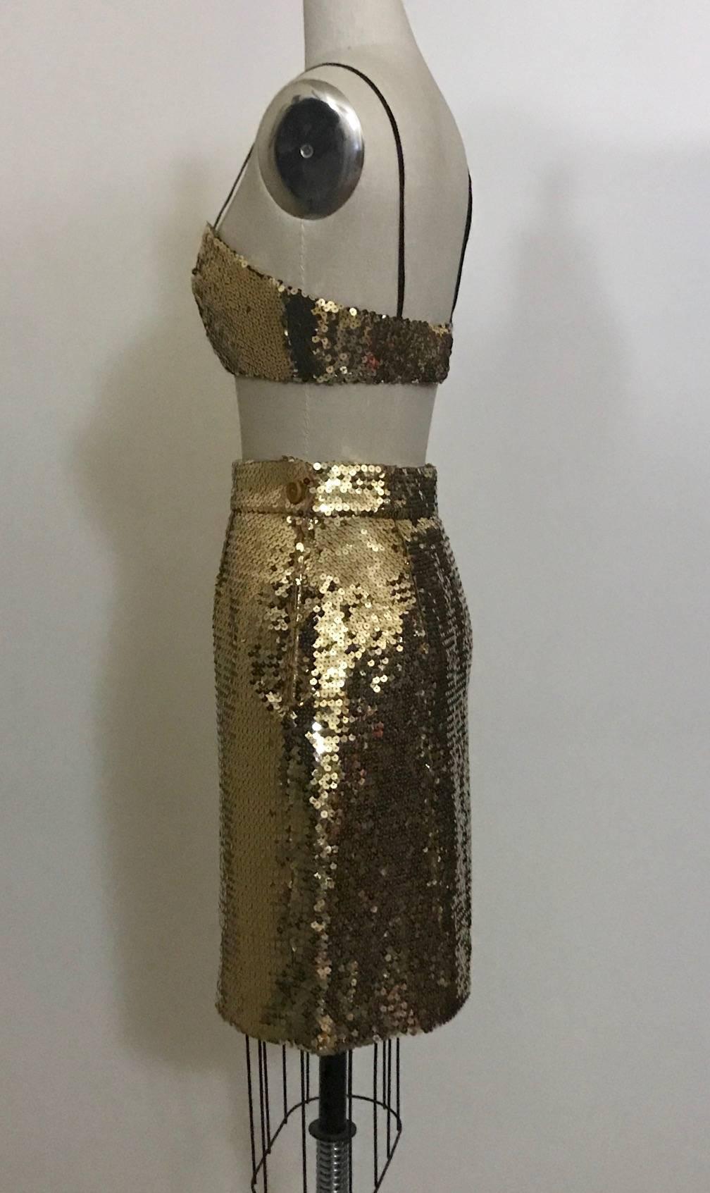 Early 1990s gold sequin cropped bustier and matching skirt by Franco Moschino. Bustier has thin black straps that can be worn or tucked in and fastens with hook and eyes at back, lined in black. Skirt fastens with side zip and snap, decorative