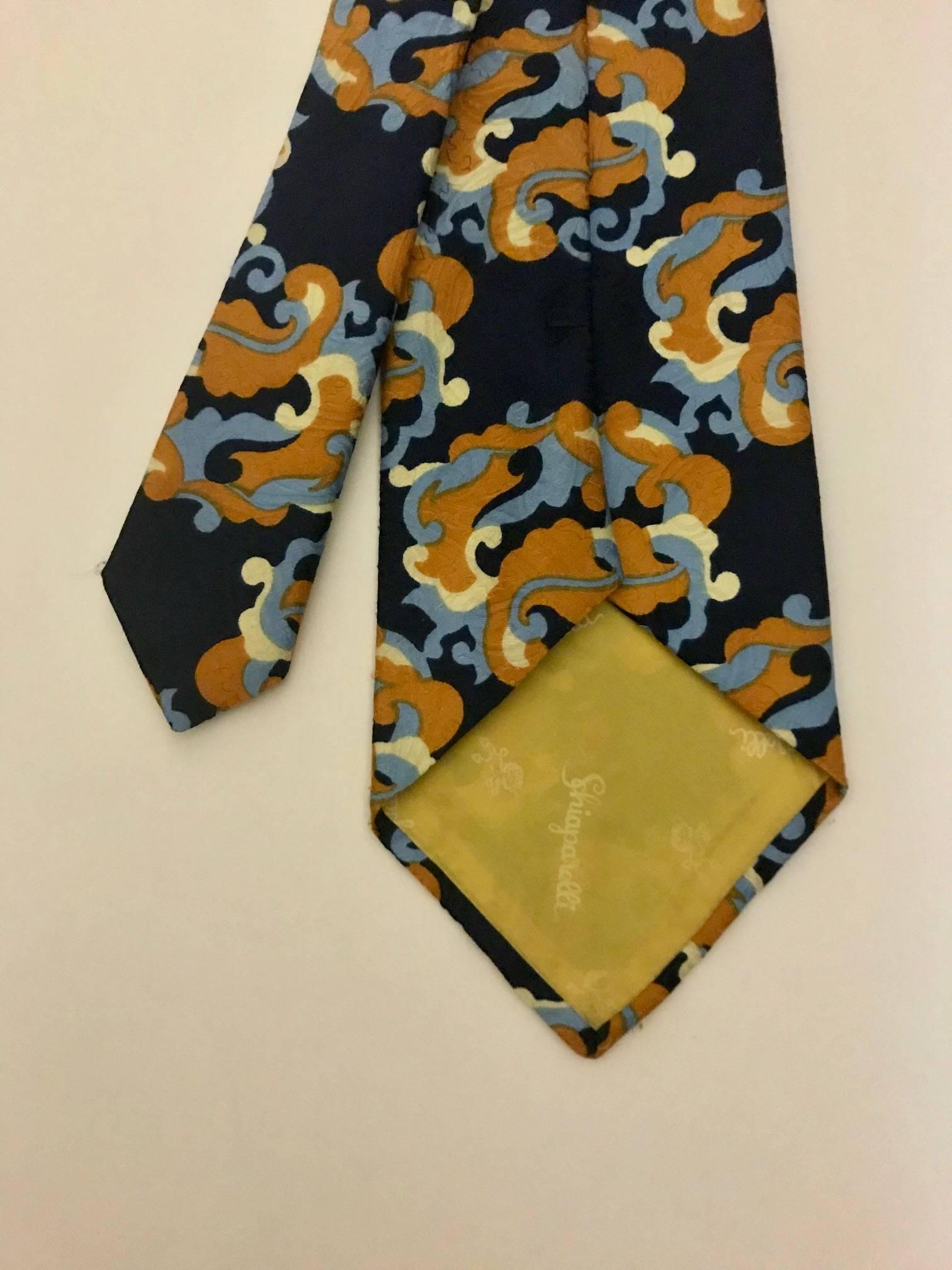 Schiaparelli vintage 1960s dark blue textured tie with light blue, gold and white paisley pattern throughout. Gold embroidered poodle with topcoat logo at bottom. Lined in gold 'Schiaparelli' signature fabric with poodle logo