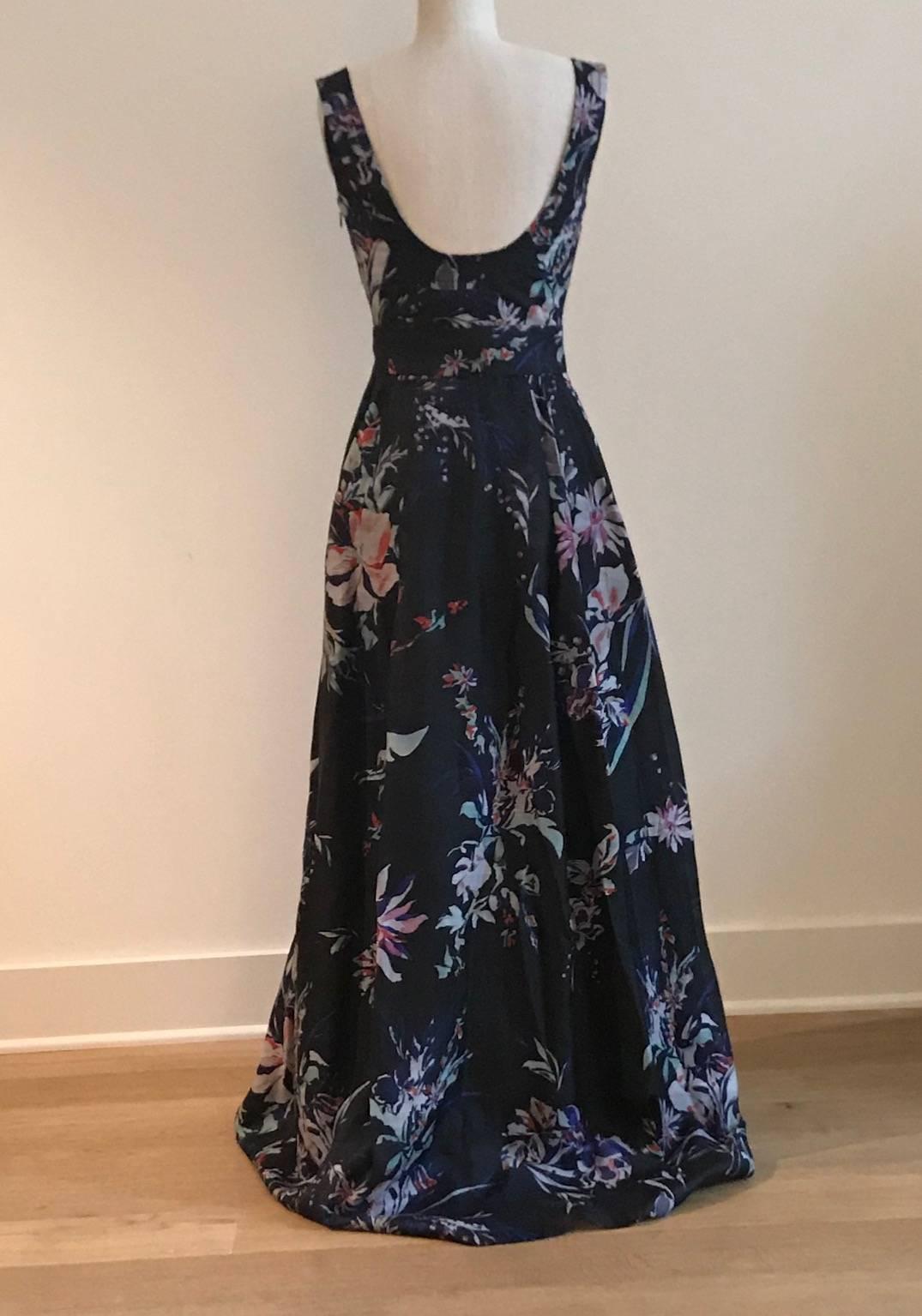 Christian Lacroix black full length dress with seamed trim detail at bust and straps and scoop back. Ivory, fuchsia, and blue and violet floral print throughout. Slit pockets at front side. Tie belt is fastened at back waist. Side zip and hook and