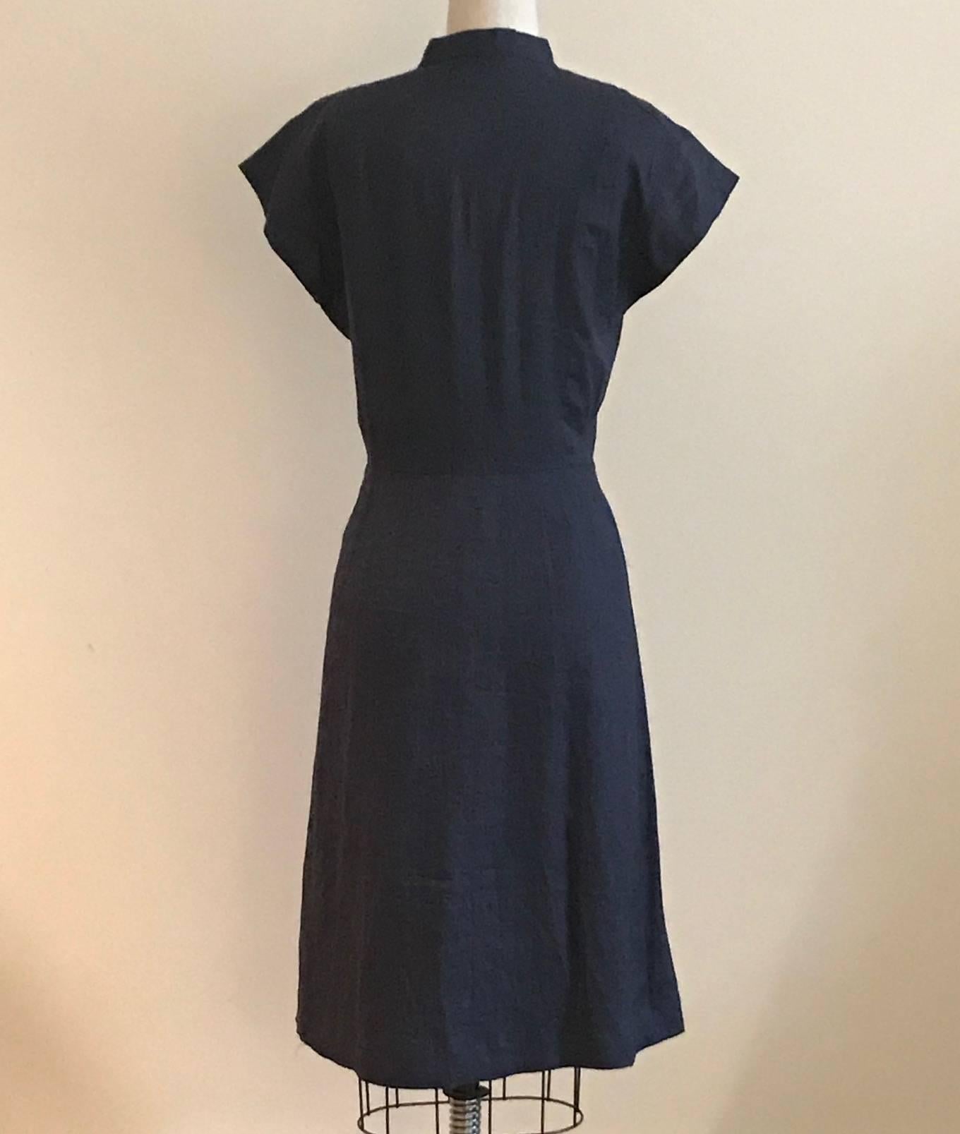 Sorelle Fontana dark blue short sleeve button front shirt dress. Pleating at front skirt. Patch pockets at chest. Navy plastic buttons with a snap at waist. Lined at skirt.

Style seems very 1940s, but may be later. 'Sorelle Fontana, Alta Moda