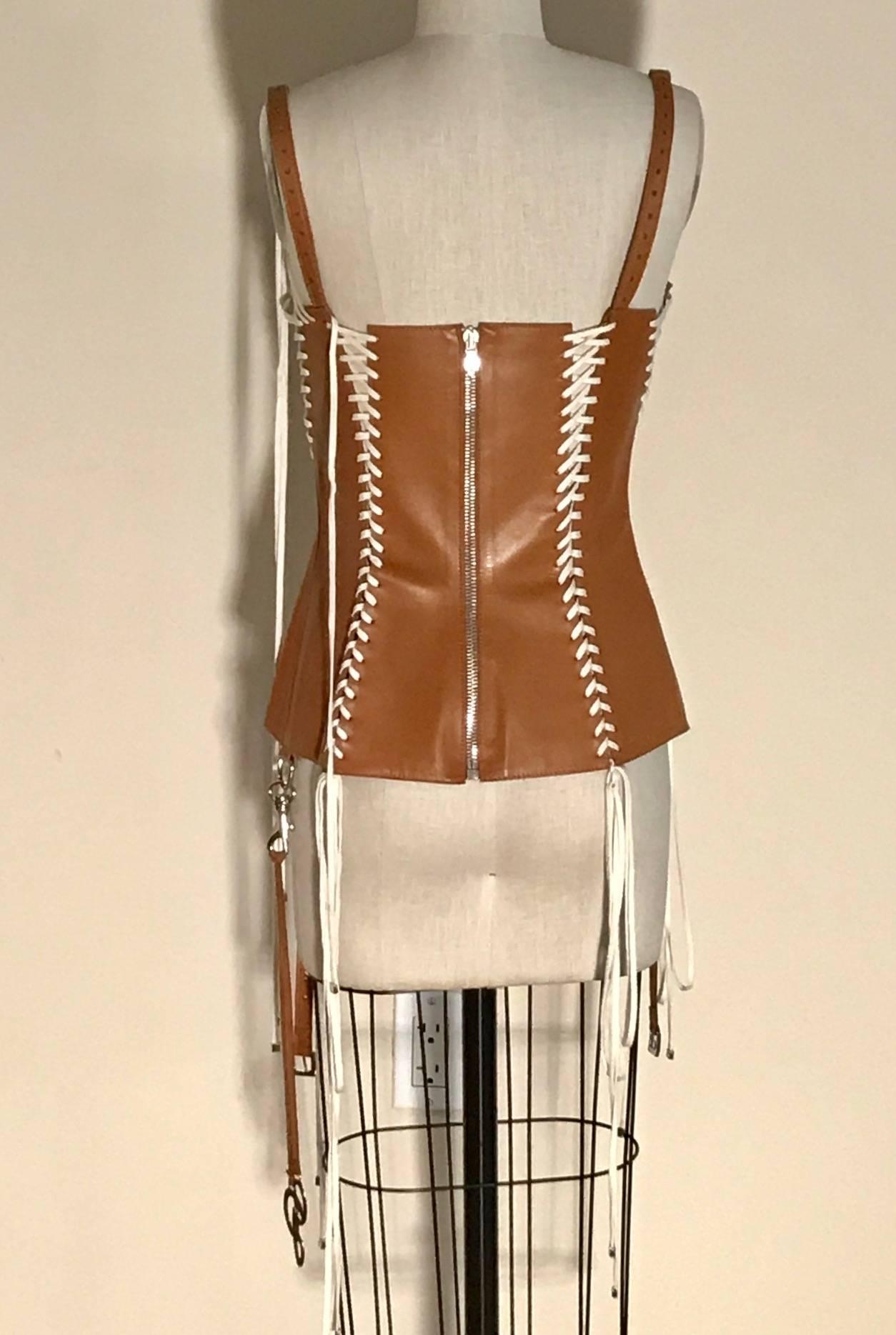 Dolce & Gabbana lambskin leather corset top in a caramel cognac color with white lacing details finished at ends with silver hardware. Asymmetrical Hanging 'DG' logo hangs on leather straps from snap hook at side. Zipper at back. Signed 'Dolce &