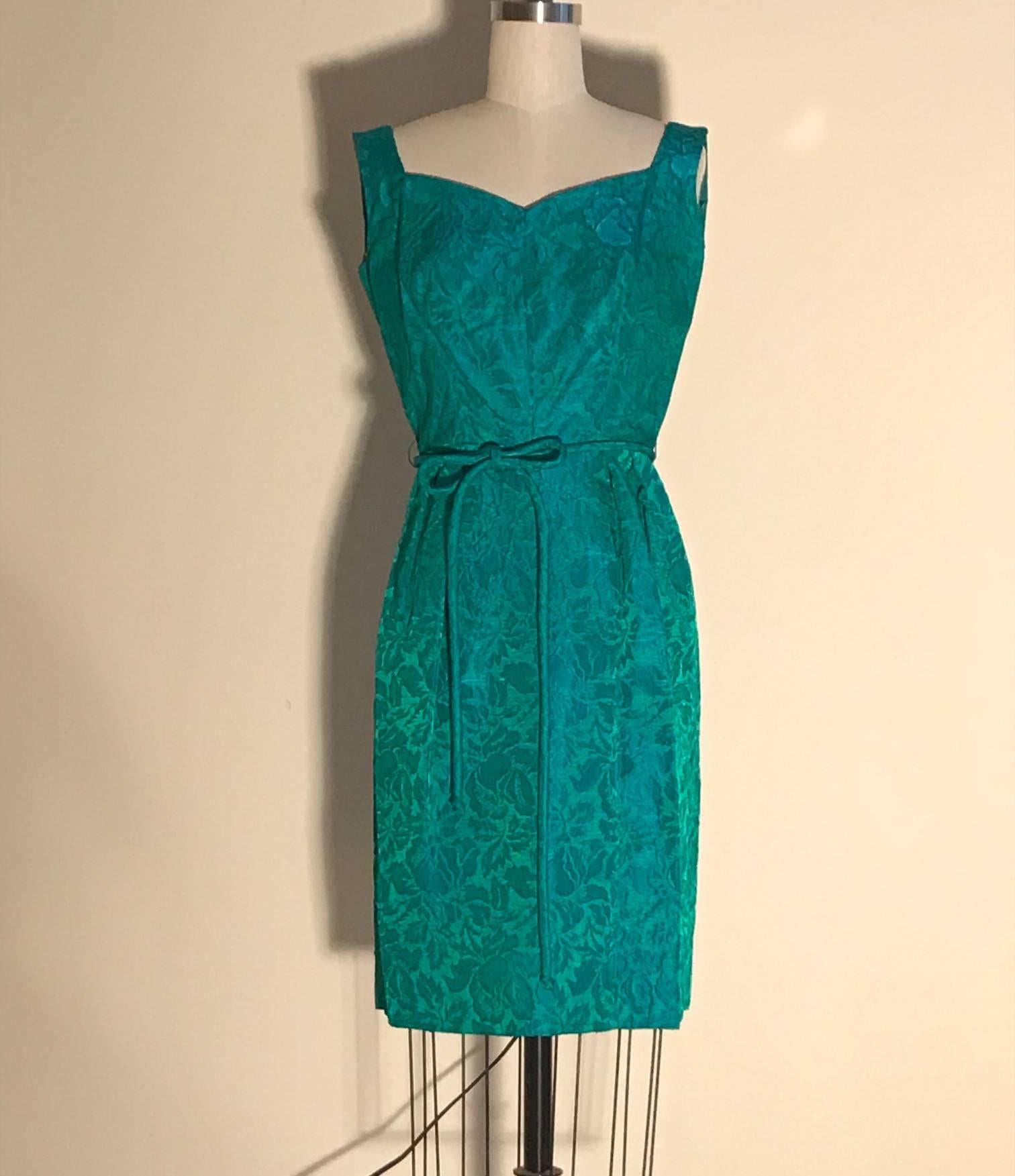 Joseph Magnin vintage 1950s blue and green floral jacquard shift dress in green with blue undertones. Tie belt at waist, back zip and hook. Short sleeve matching coat has high side slits/open sides with a single button closure and hook and eye at