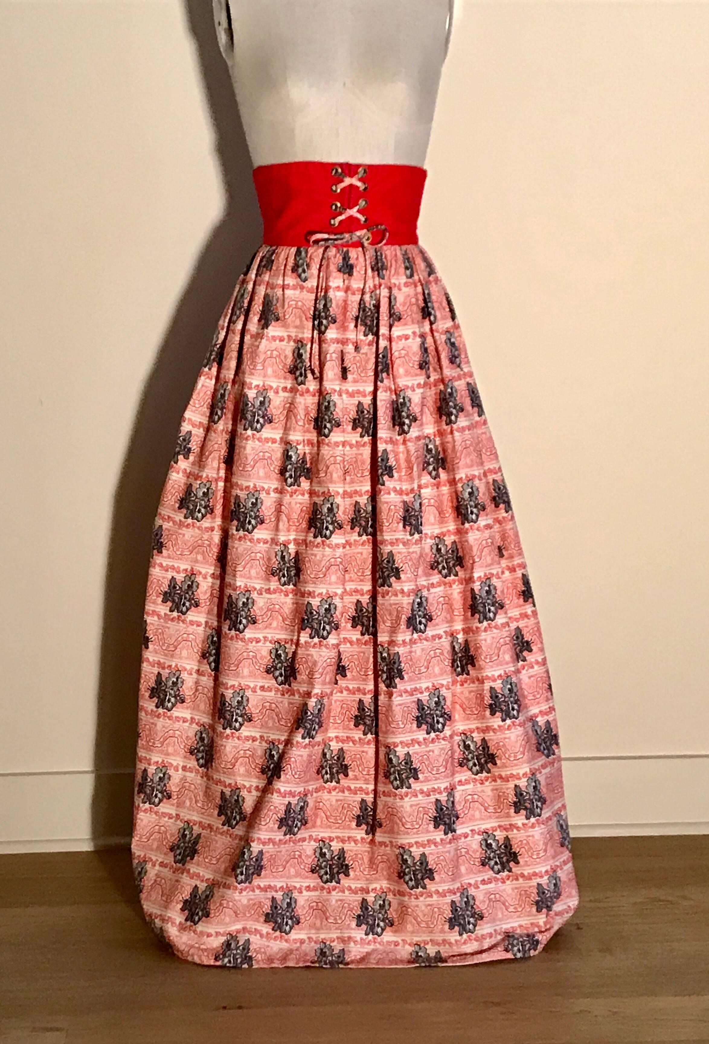 Vintage 1960s style Bohemian full length skirt (actual decade unknown.) Red, white, and black full maxi skirt in a striped floral print with grommeted lace up detail at front center waist and three red buttons at back waist. Center back zip. 

No