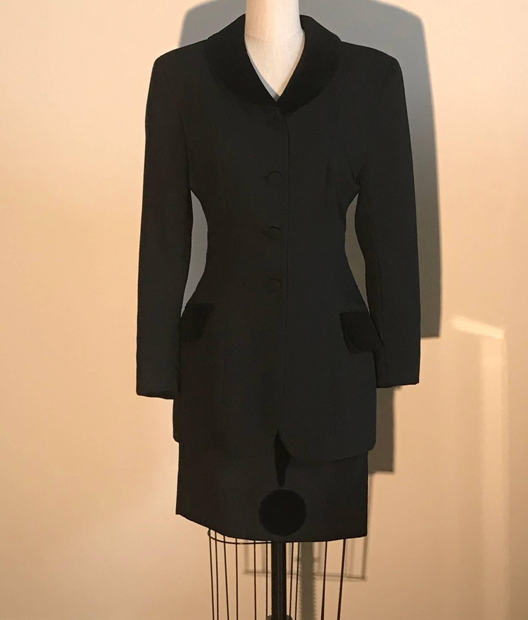 Moschino Cheap and Chic vintage 1990s black suit with velvet accents. Jacket features velvet collar and pockets, while skirt features a question mark that wraps around the skirt. Velvet loop at bottom of collar, possibly for holding a scarf. Jacket