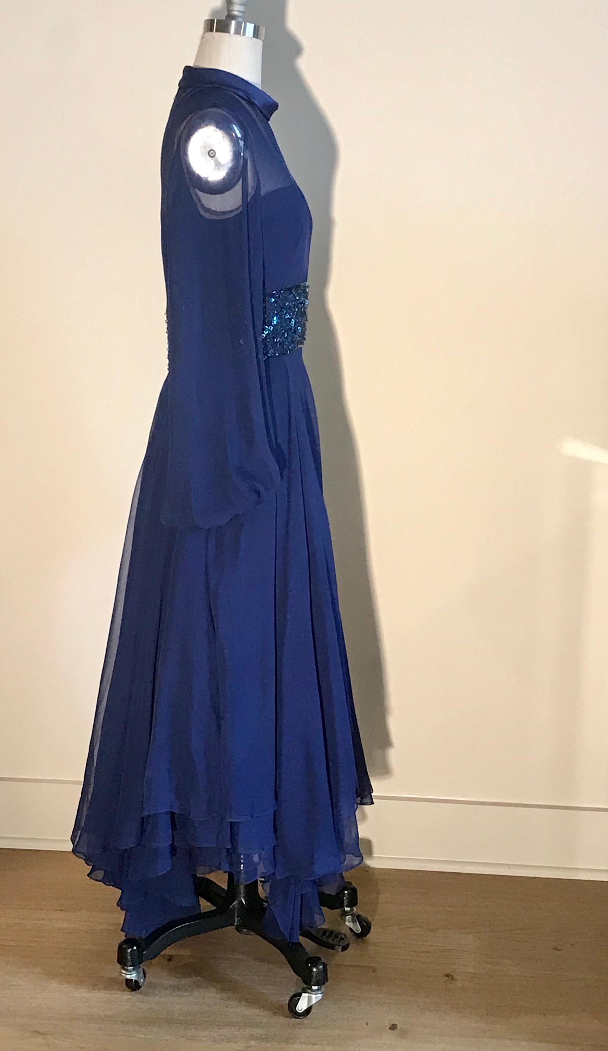 William Travilla vintage cobalt blue dress (estimated 1970s) featuring sheer detailing and beaded embellishment at waist. Amazing layered skirt has tons of movement. Wide sheer sleeves are banded at wrist to create volume. Nude lining at top. Back