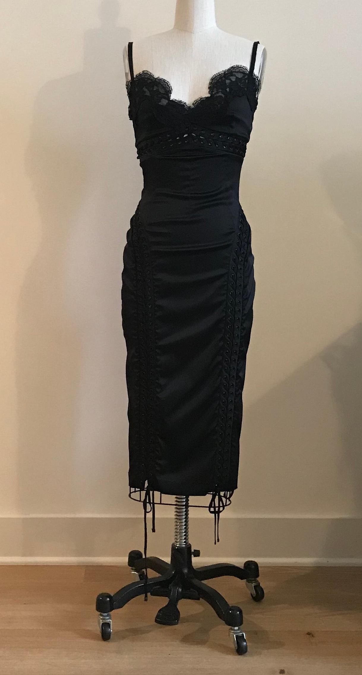 Dolce & Gabbana black satin midi dress with lace trim at chest and peekaboo corsetry inspired lacing at bodice and skirt. Back zip. Zips to just below buttocks and then fastens with hook and eyes so you can create an adjustable back slit if desired.