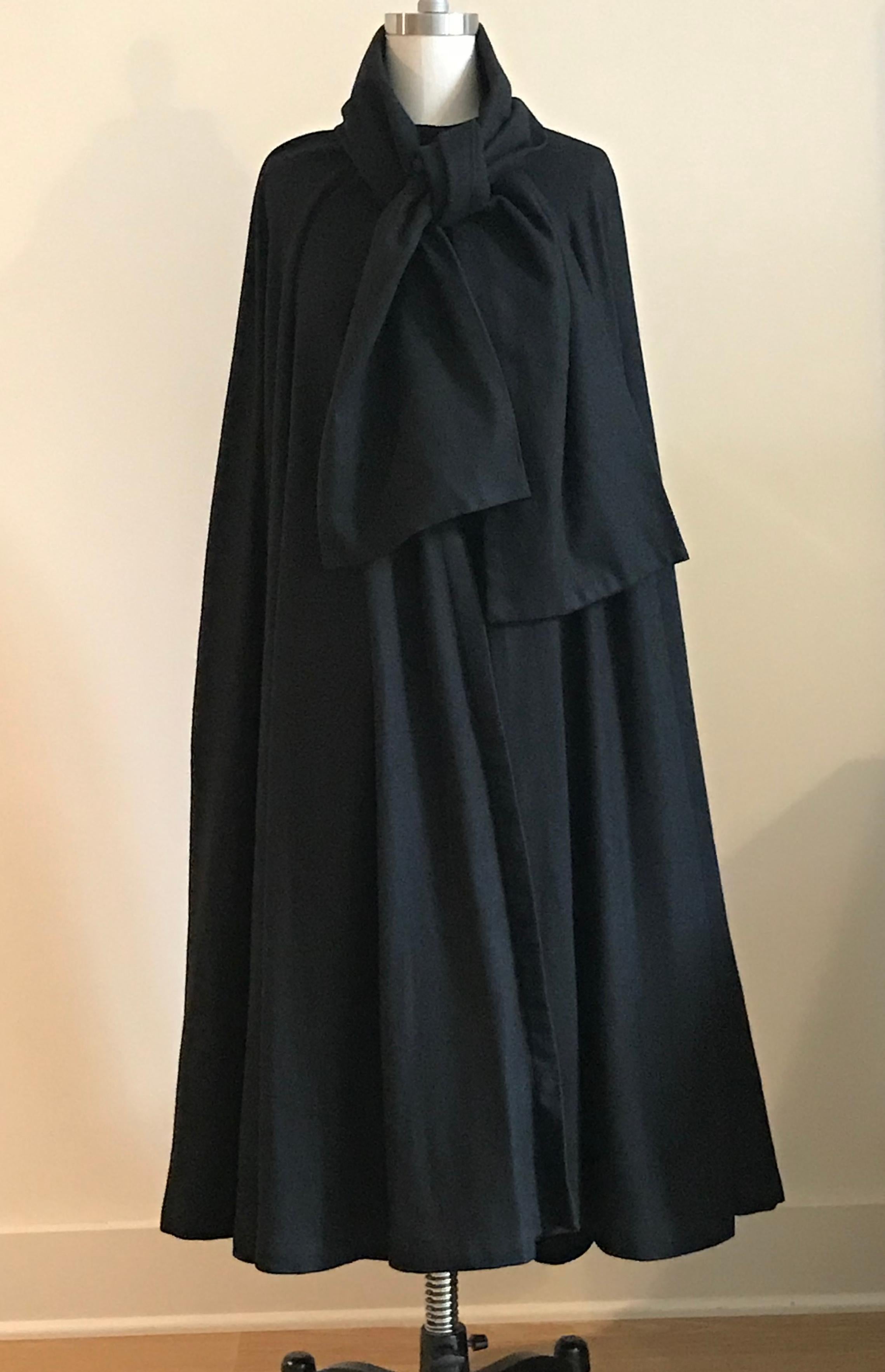 Geoffrey Beene vintage 1970s black cape with a faint herring bone weave. Closes at neck with a snap and hook. Wide scarf detail at collar Can be tied and let hang, or tucked in around neck to create a more sculptural look. Hits between knee and
