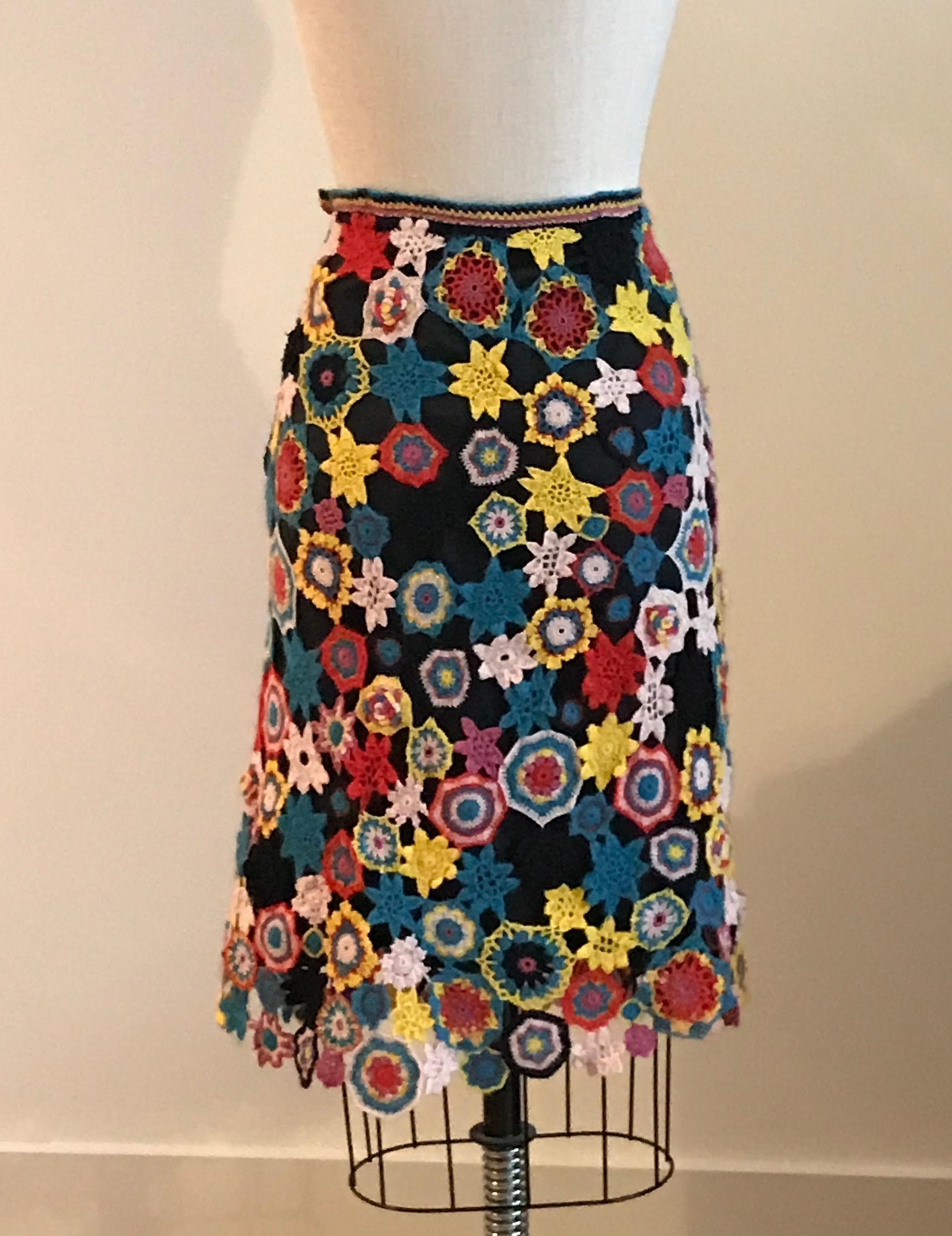 Christian Lacroix retro 1970's inspired crochet patchwork skirt in vibrant tones of red, pink, blue, and yellow on a black background. Open work crochet with attached black slip underneath. Side zip and button. 

100% wool. 
Lining feels like