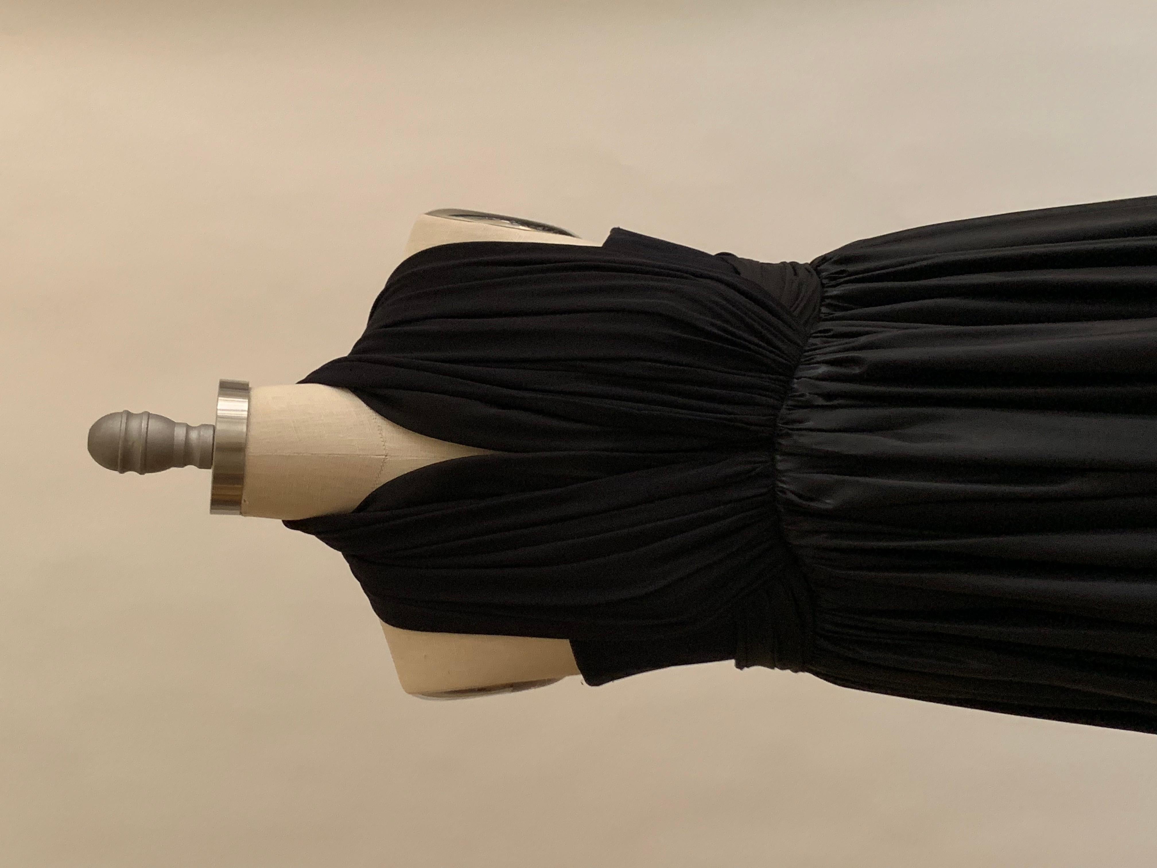 Balenciaga 2004 black dress features a black mesh bodice with two sets of halter straps that attach at waist. Another piece of draped fabric fastens at waist as belt. Skirt has a liquid like sheen and ruffle bottom. Fastens at side with hook and eye