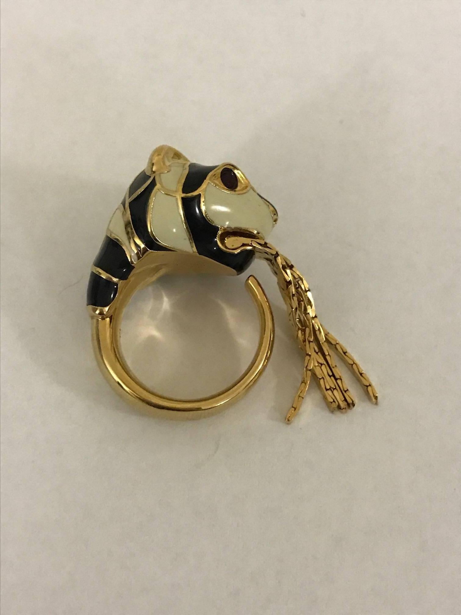 Gold tone Gucci ring with large black and white enamel tiger detail. Red crystal eyes. Four pieces of gold fringe dangle from the tiger's mouth.

Signed 'Gucci' at interior and side.

Made in Italy.

Size 6.5.
Band is approximately 7 mm wide,