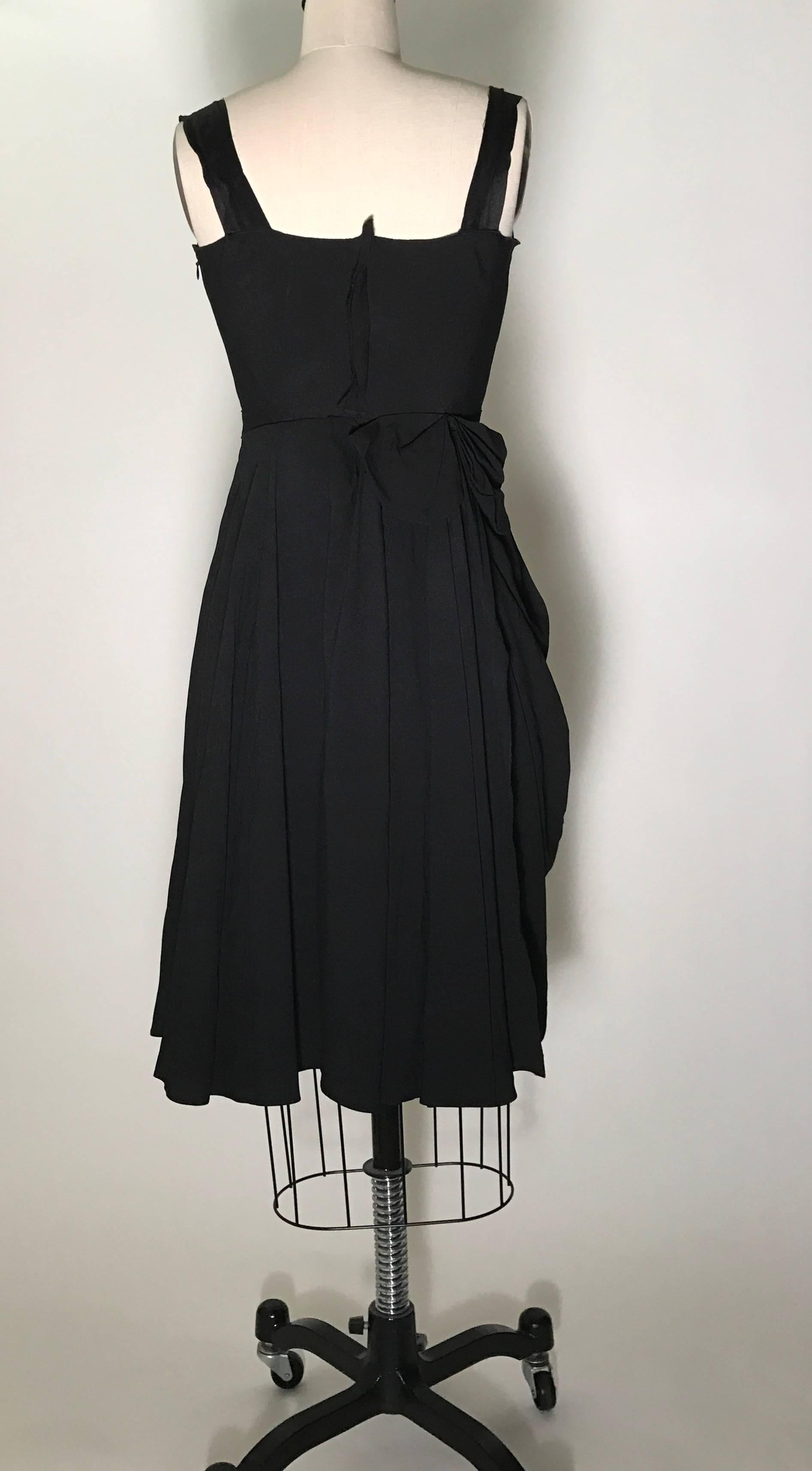 Prada black strapless dress with sweetheart neckline and rosette detail at strap. Asymmetric draped skirt with bow at back. Side zip and hook and eye. Grosgrain reinforcement at interior waist fastens with hook and eyes.

57% acetate, 43% viscose.