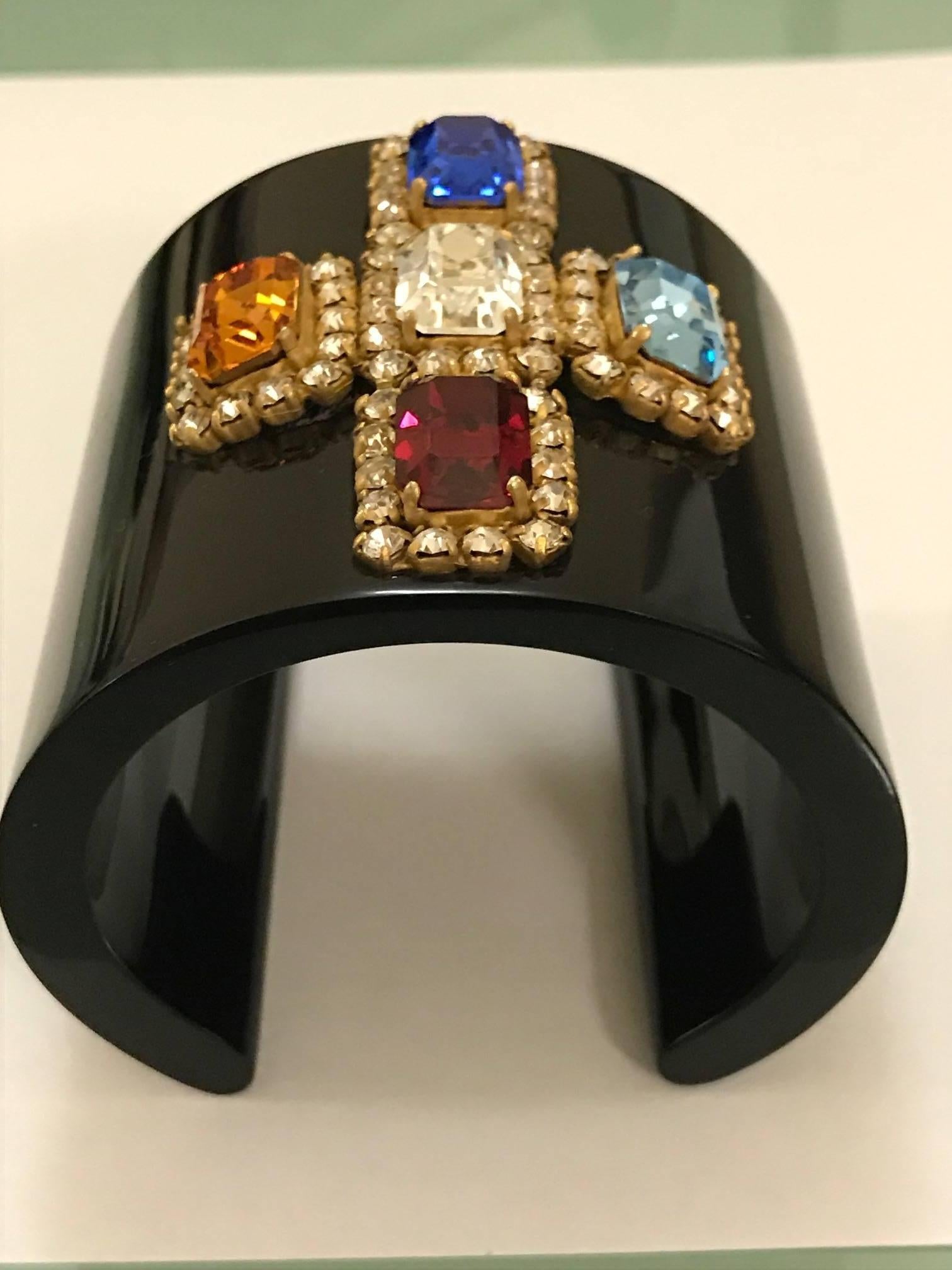 Chanel black resin cuff bracelet featuring a multicolored crystal cross design in gold tone setting from the Spring 1995 collection.

Circumference measures around 5" at interior.
Width is approximately 2.3".

Signed (copyright) Chanel