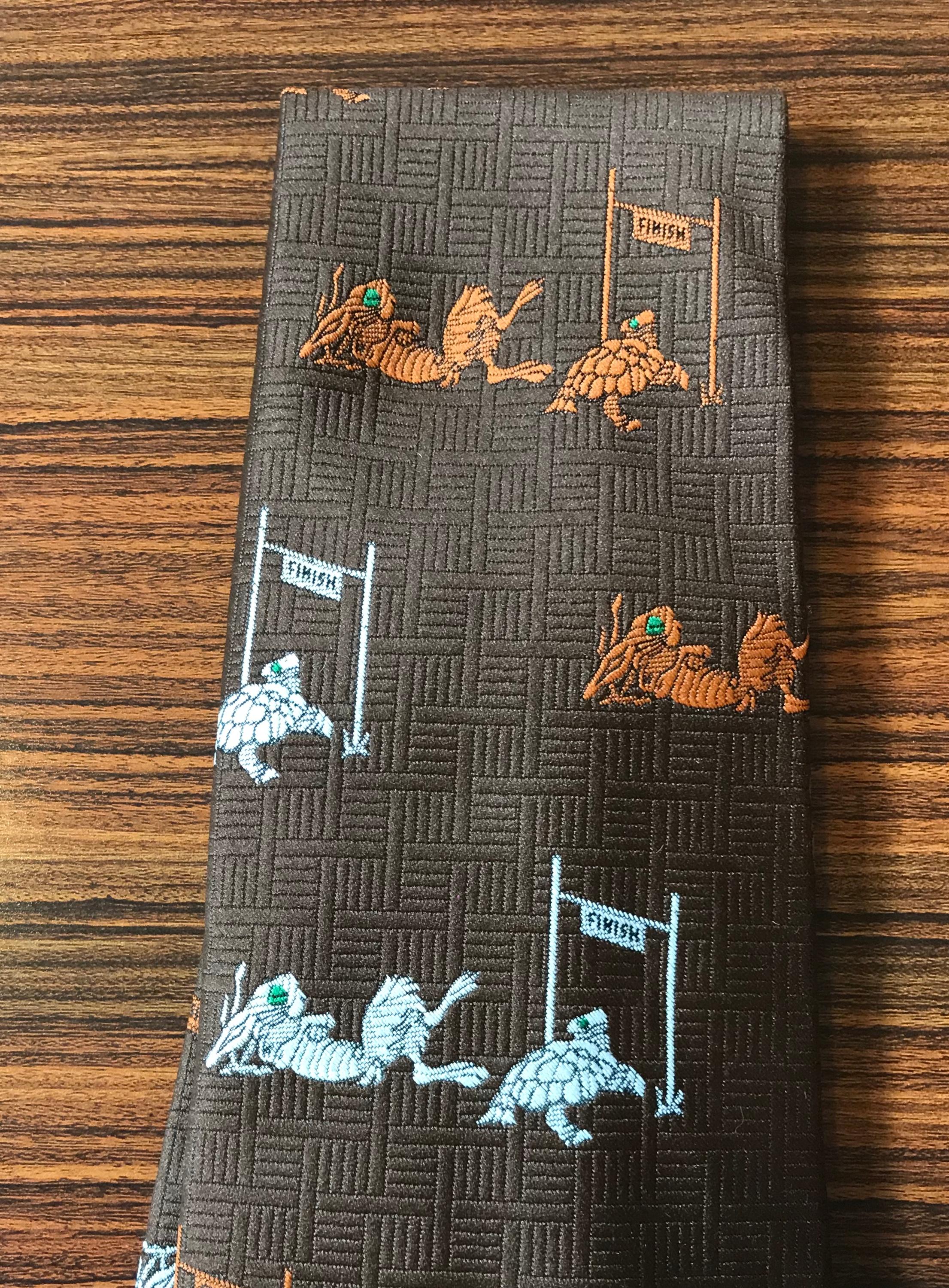 Rather bizarre Schiaparelli 1970s wide brown tie featuring the final scene from the fable The Tortoise and The Hare. The tortoise crosses the finish line while the hare naps nearby. Signed Schiaparelli at pink lining and at tag.

Measures 4 1/2