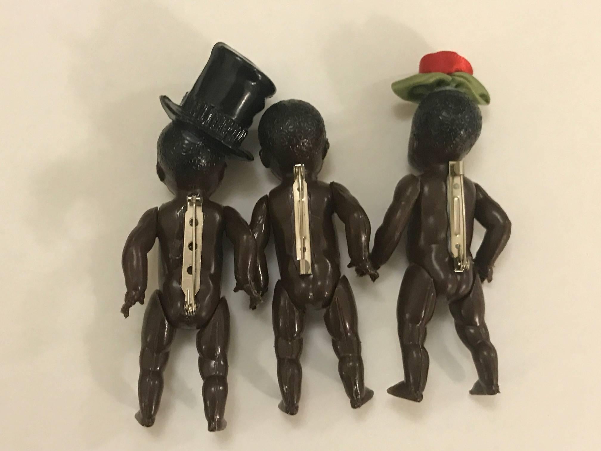 Set of three Patrick Kelly 1980s baby doll pins, one plain, one with a black top hat, and one with a rose bud topper. 

Patrick & volunteers would sit in the studio adding pins and accessories to tons of these dime-store plastic baby dolls to give