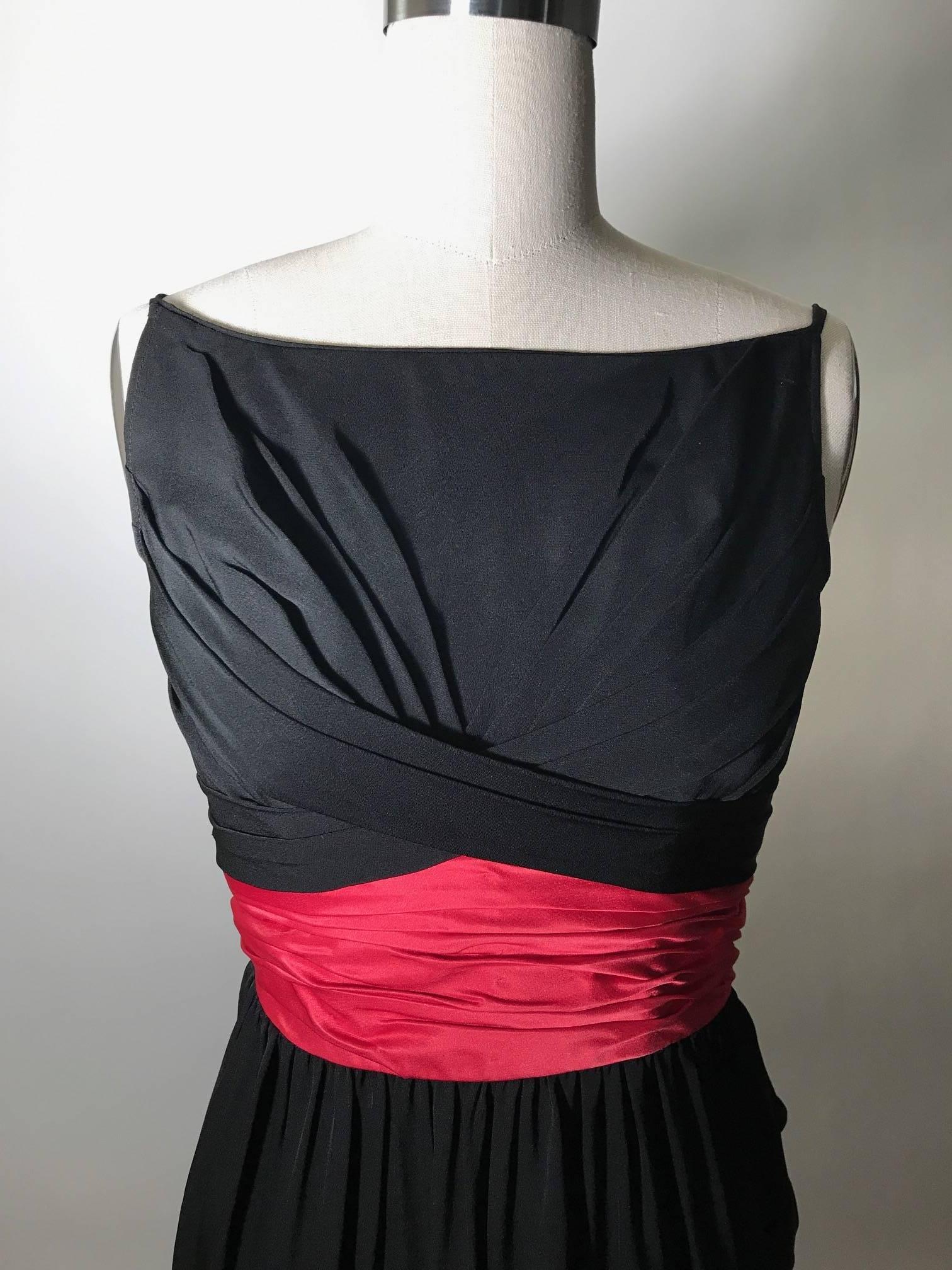 Ceil Chapman vintage 1950s black boatneck dress with pleated detail at front and back bodice. Skirt is gathered at deep pink/red attached waist sash/cumberbund. Back zip (there are hook and eyes along back zip to conceal the zipper, but we could not