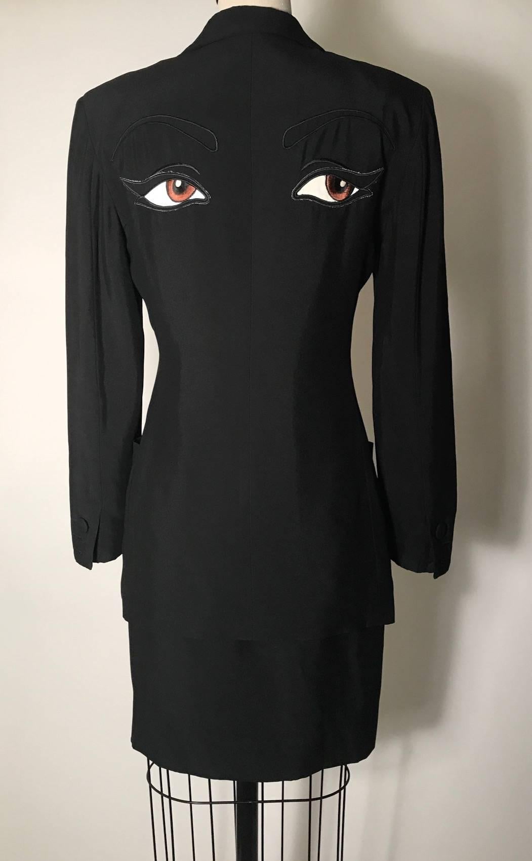 Moschino Couture vintage  'The Eyes' skirt suit from Franco Moschino's Spring 1990 collection. Black blazer features an appliquéd and embroidered pair of eyes at back. Strong, slightly padded shoulder, pockets at front, cloth covered buttons at