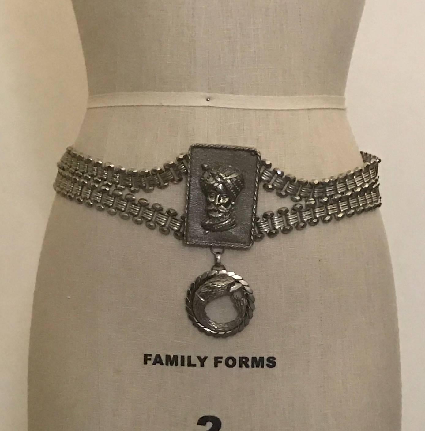 Vintage Christian Dior 1970s (estimated) silver belt featuring a turbaned sultan medallion at front and a hanging snake like creature with an eagle's head. Etched & faceted silver chain. Fastens with hook at side.

Signed 'Christian Dior' at