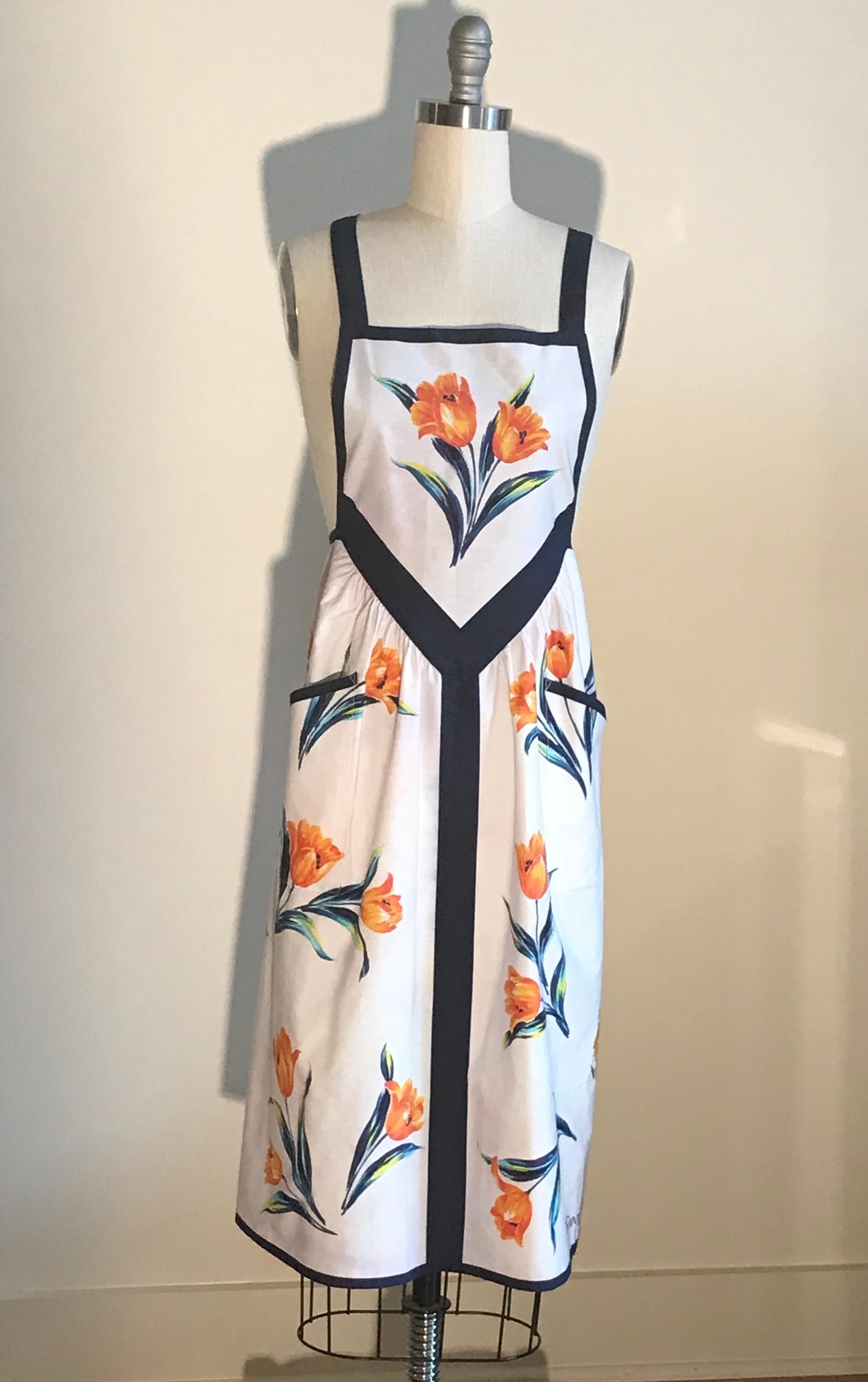 Vintage Yves Saint Laurent apron by the Japanese Apron Association. White apron with orange blue floral print throughout. Yves Saint Laurent logo at side bottom. Criss cross straps button at back. Back tie. 

Could be worn as an apron, or even worn