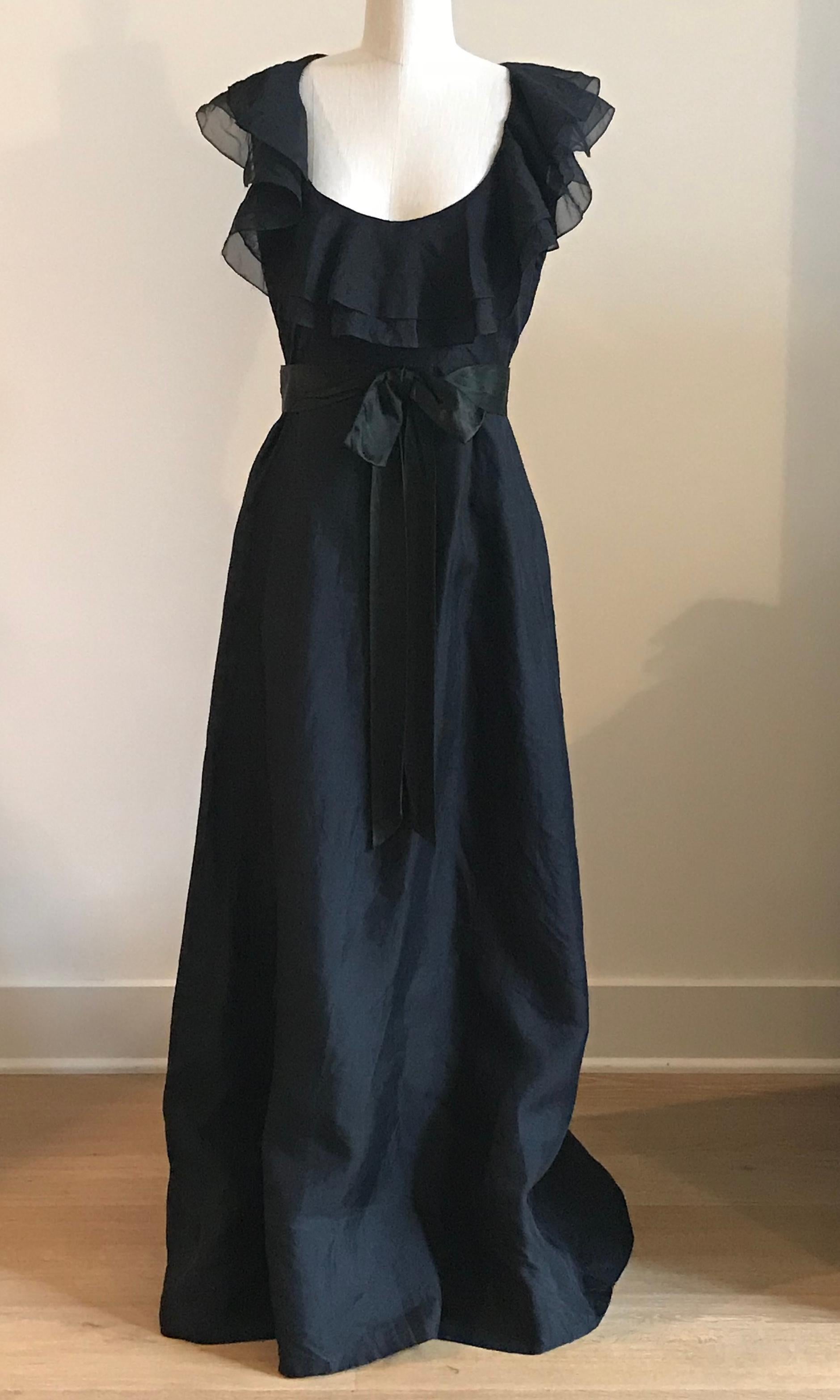 Vintage 1960s Sarmi black floor length dress with a low cut neck surrounded by a layered ruffle and a ribbon bow belt at waist. Back zip.

No content label, feels like a mid-weight semi-sheer organza.
Fully lined.

No size label, best fits S/M. See