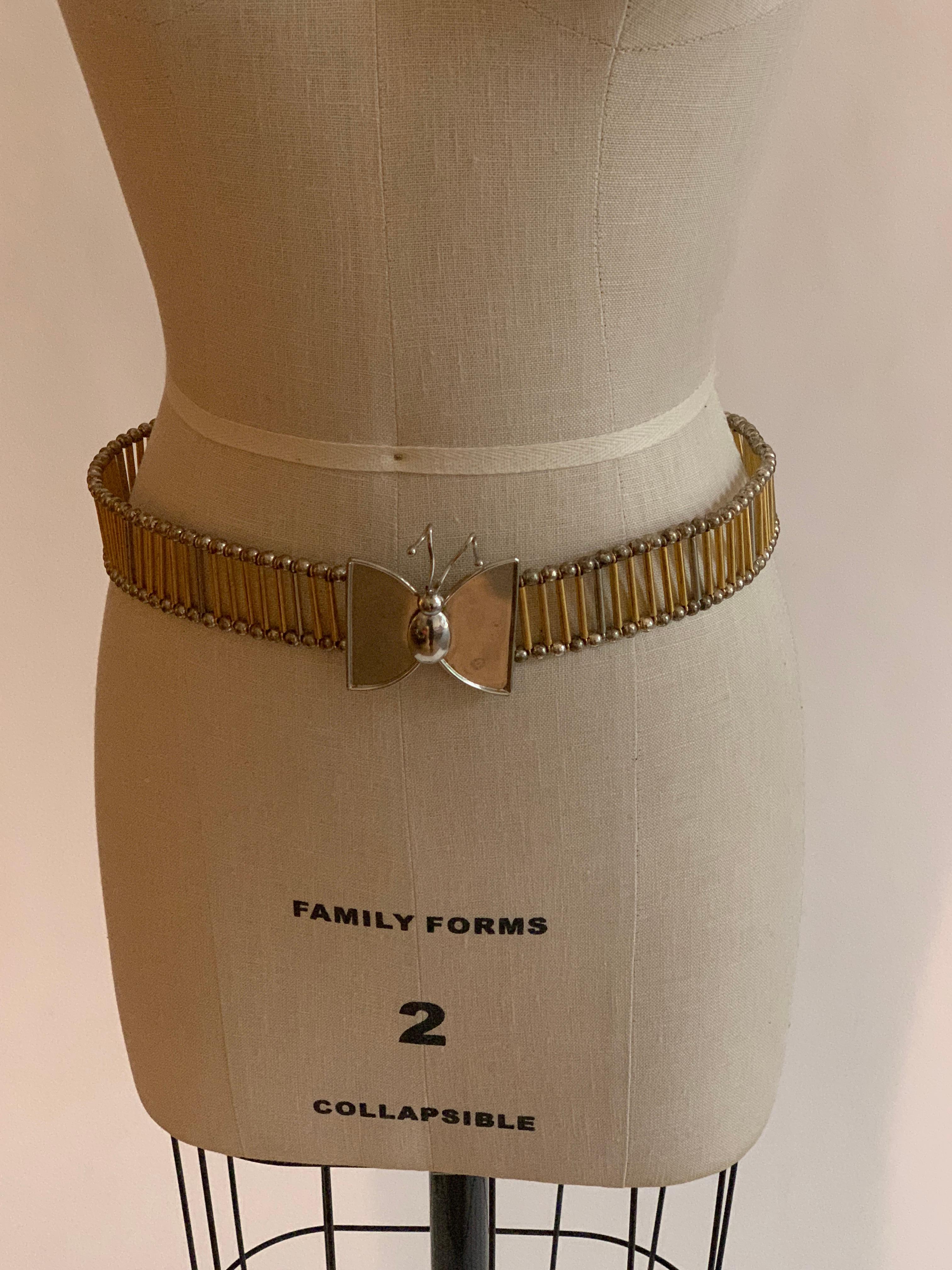 William De Lillo metal butterfly belt in silver and gold tones. Long silver and gold tone metal beads connect  silver ball pieces at edges. Fastens with two hooks at back of butterfly.

Stamped 'de Lillo' at butterfly back.

Adjustable up to 30
