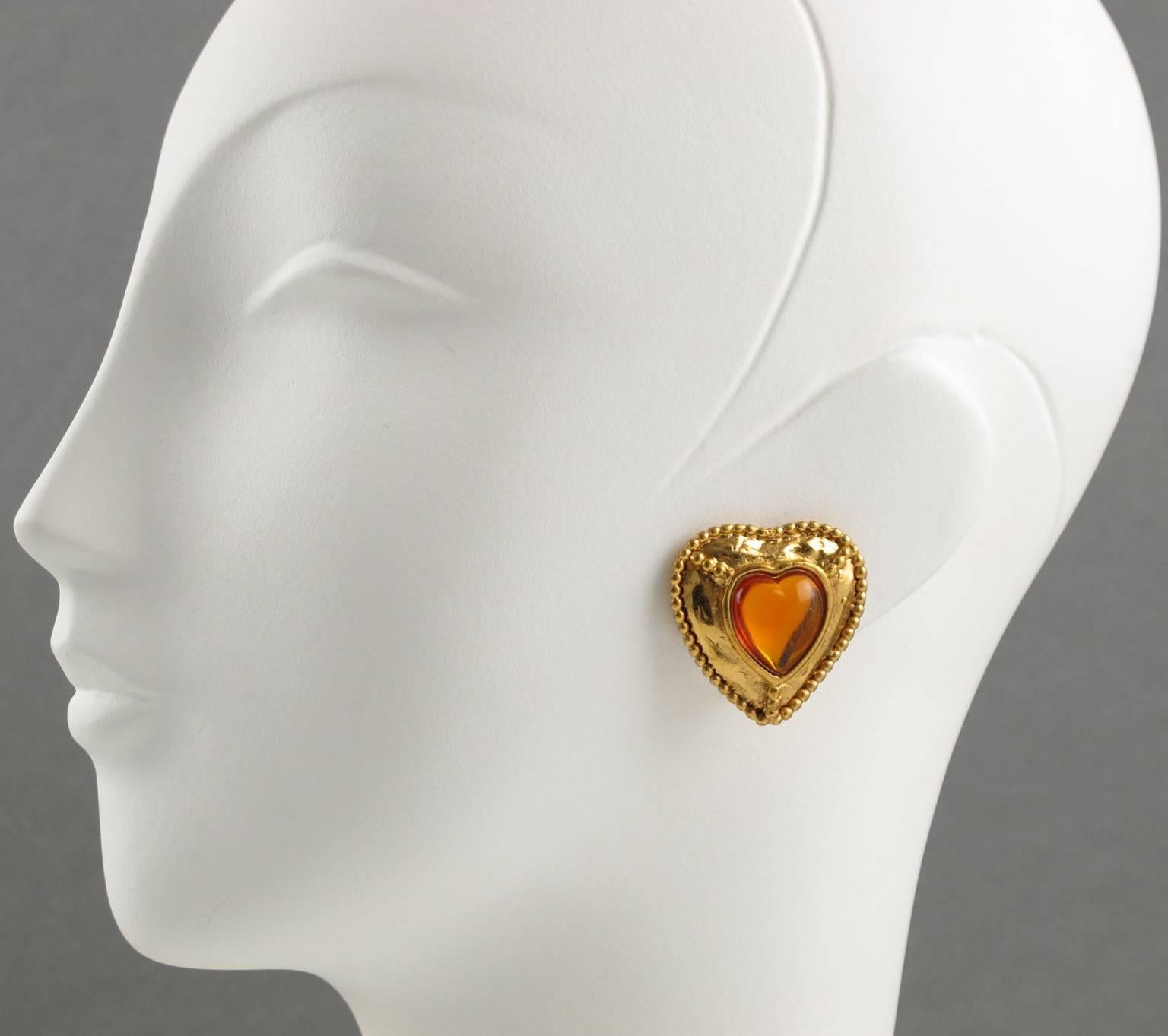 YVES SAINT LAURENT Paris signed clip on earrings. Modernist heart shape, shinny gold tone metal with texture and carving ornate with orange resin cabochon, heart shaped. Signed at the back with YSL pierced logo on clip and engraved underside: