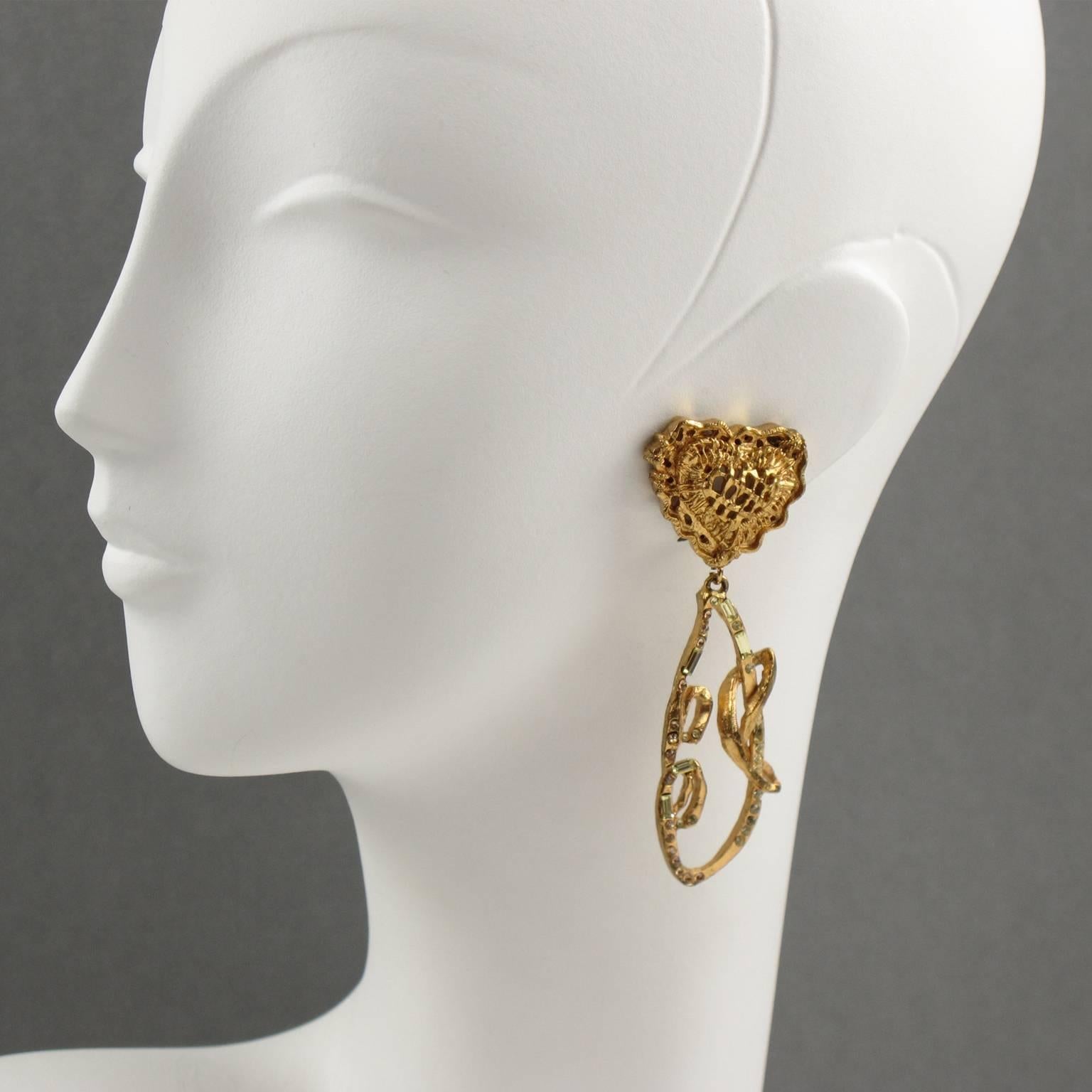 CHRISTIAN LACROIX Paris signed clip on earrings. Elegant modernist gilt metal dangling shape, metal all textured, featuring a pierced heart and lace dangling element, all paved with shaped clear and champagne rhinestones and clip back. Signed on