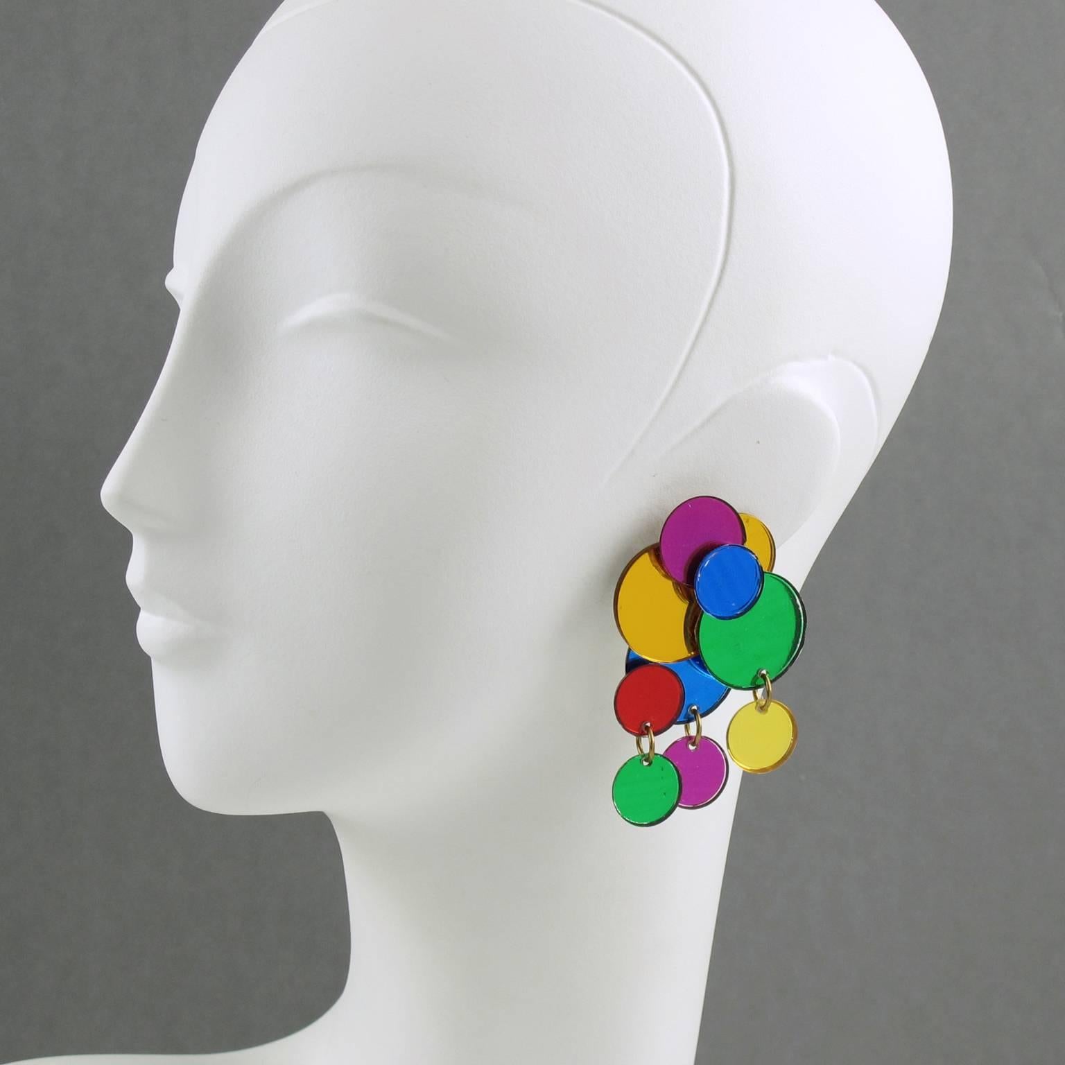 Super cool fun and funky pair of dangling clip on earrings. Cluster dangle shape with multicolor Lucite disks and charms. Mirror glittering effect and assorted colors of yellow, green, pink, blue and red. Clip back and silver color