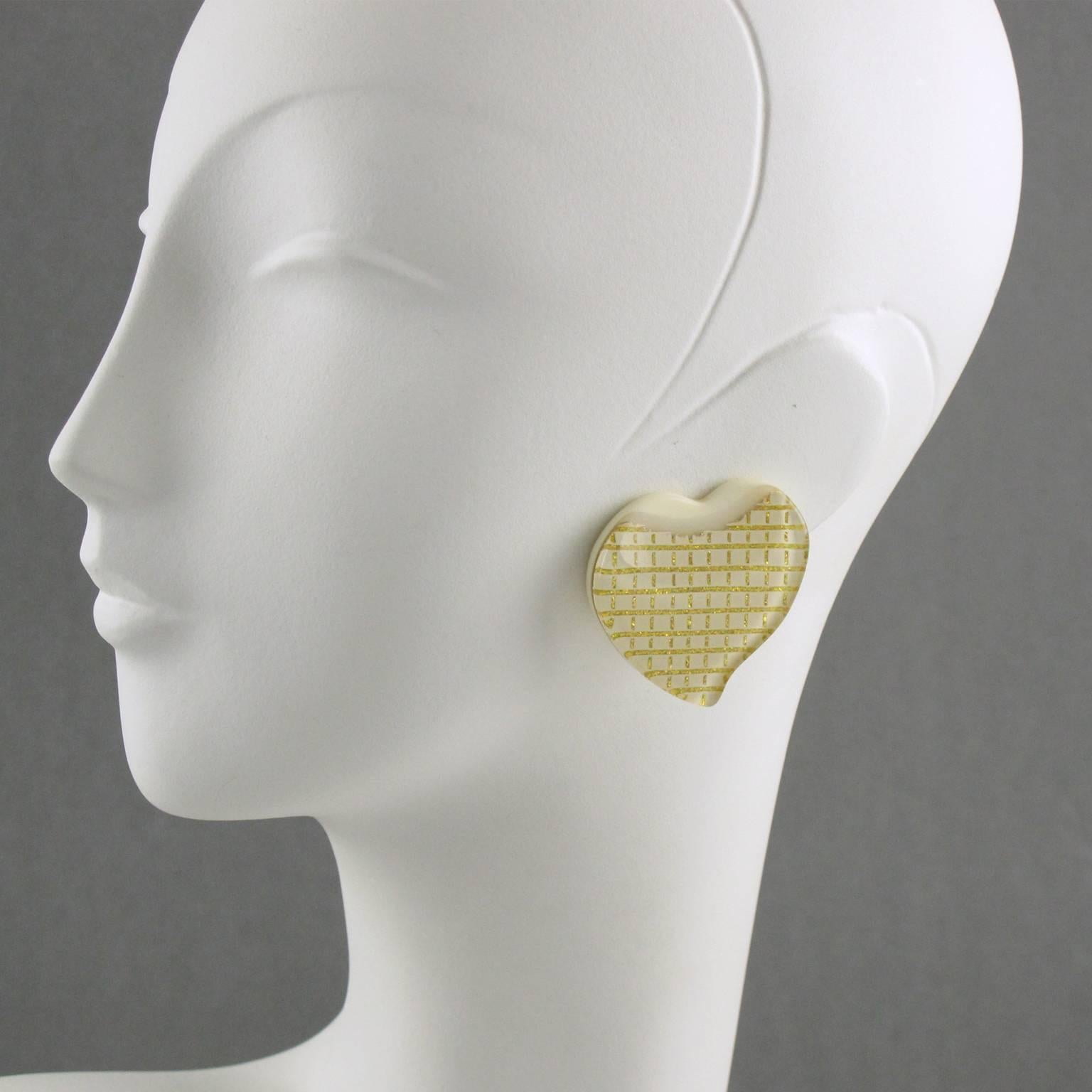 Vintage 1960s oversized Lucite clip on earrings. Large carved heart shape with lamination. Off-white color background with geometric gilt design. Excellent vintage condition.

Measurements: 1.57 in. wide (4 cm) x 1.57 in. high (4 cm)