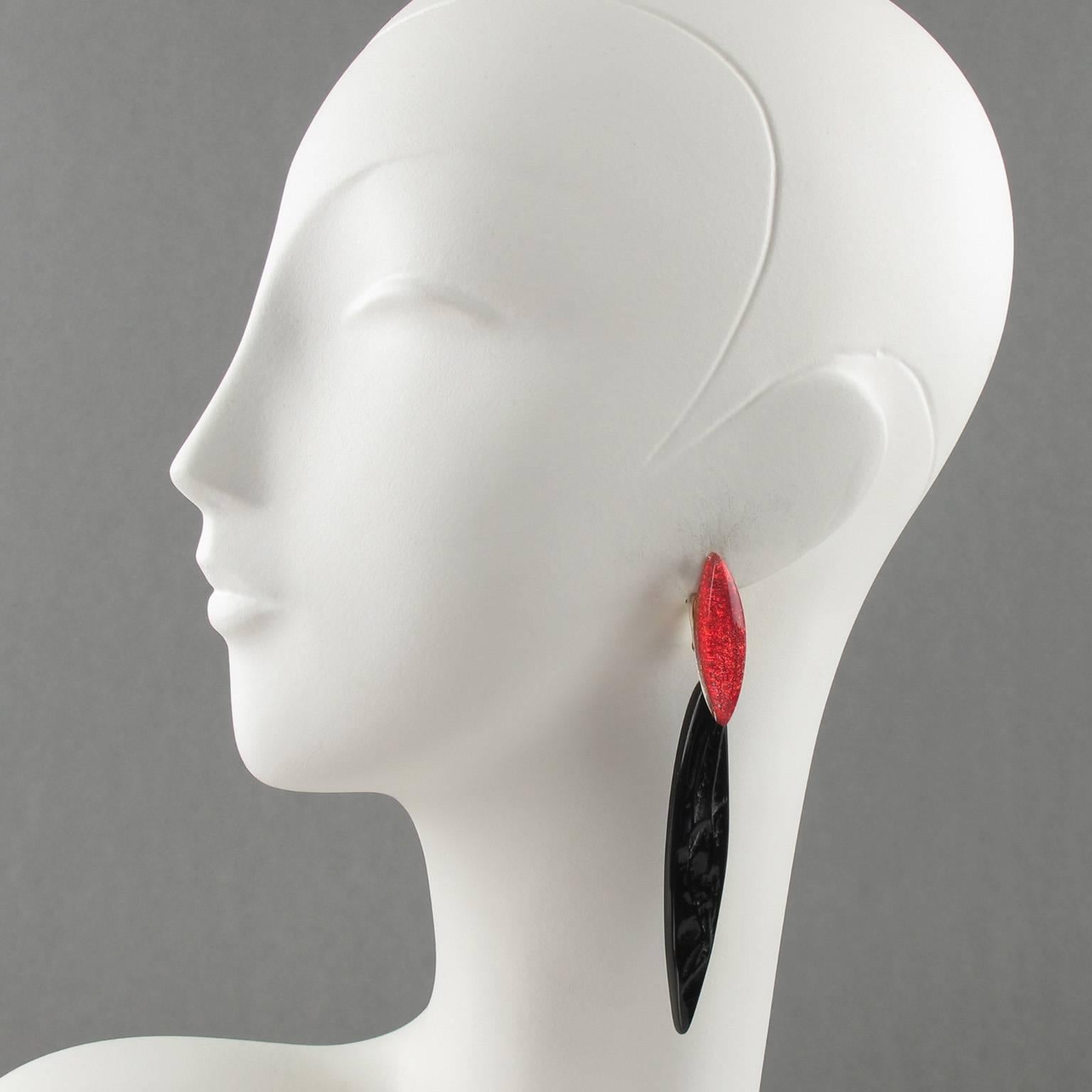 Stunning artisan designer oversized shoulder duster clip on earrings. Minimalist slim design with dangling shape, black resin in free-form carved design with textured pattern, compliment with long drop clear lucite element with red glitter flakes