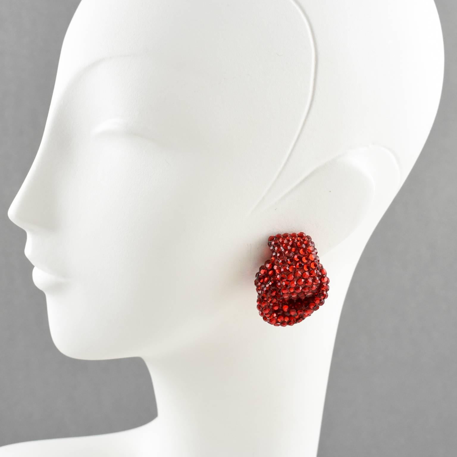 Classic statement clip-on earrings designed by Richard Kerr in the 1980s. They are made up of his signature pave rhinestones. Featuring dimensional knot shape all covered with colorful crystal rhinestones on red resin background frame. Vivid ruby