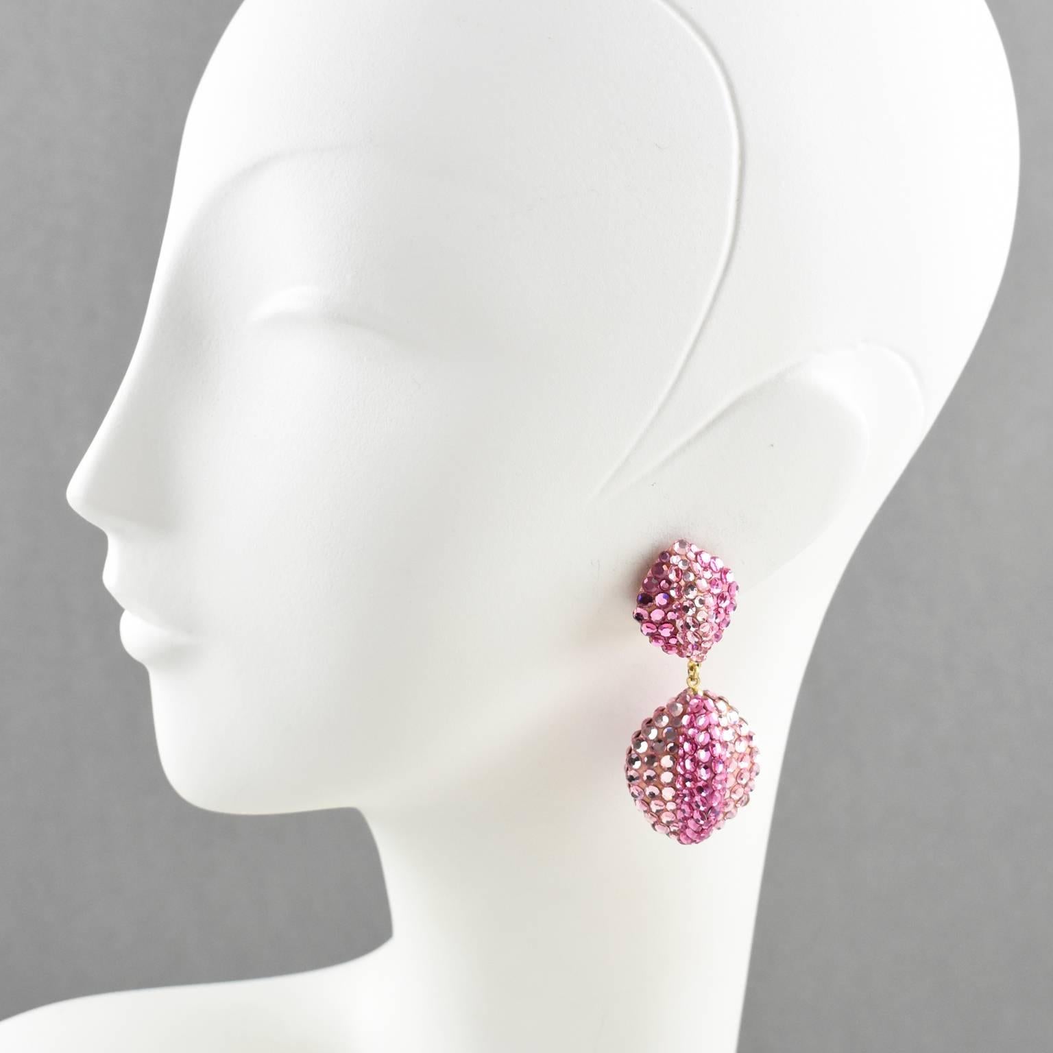 Stunning statement clip-on earrings designed by Richard Kerr in the 1980s. They are made up of his signature pave rhinestones. Featuring dimensional dangling nuts shape all covered with colorful crystal rhinestones on pink resin background frame.