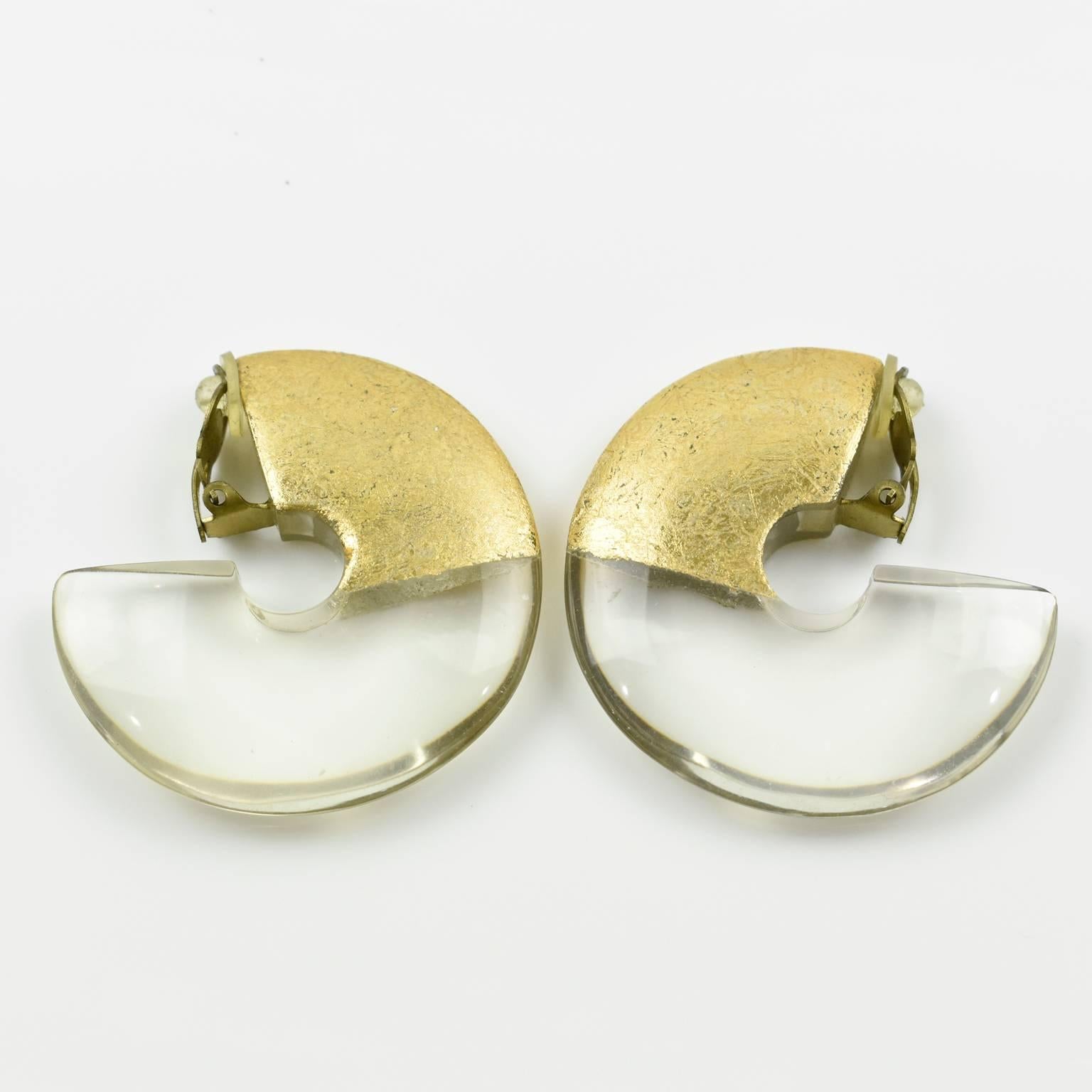 Stunning oversized clip on earrings by Gerda Lyngaard for Monies. Crystal clear Lucite and gold foil application. Marked 'Monies' on clasp. 
Measurements: 2.13 in. diameter (5.4 cm) x 0.38 in. thick (1 cm)