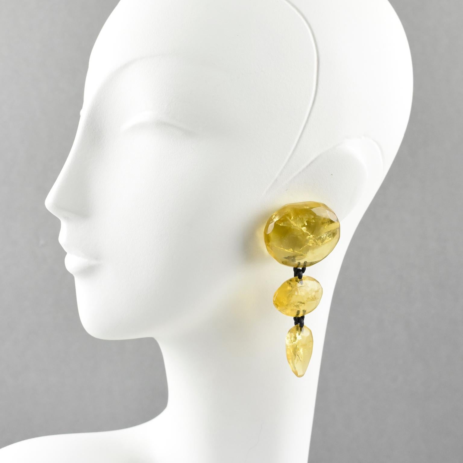 Stunning oversized clip on earrings by Gerda Lyngaard for Monies. Dangling pebble shape with golden amber Lucite or resin with inclusion. Marked 'Monies' on clasp. 
Measurements: 3.38 in. high (8.5 cm) x 1.44 in. wide (3.7 cm)