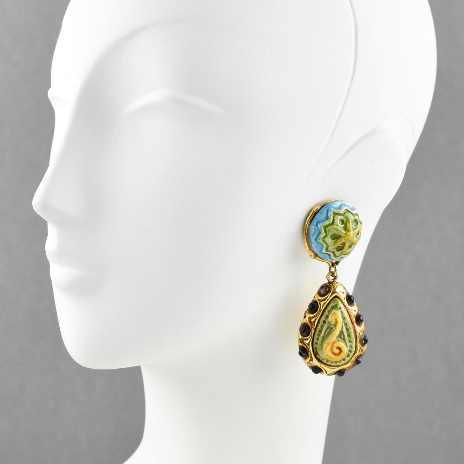 Elegant Kalinger Paris clip-on earrings. Oversized dangling shape featuring gilt resin drop with textured pattern ornate with burgundy glass beads and topped with carved ceramic elements. Ceramic cabochons have assorted colors of apple green, blue