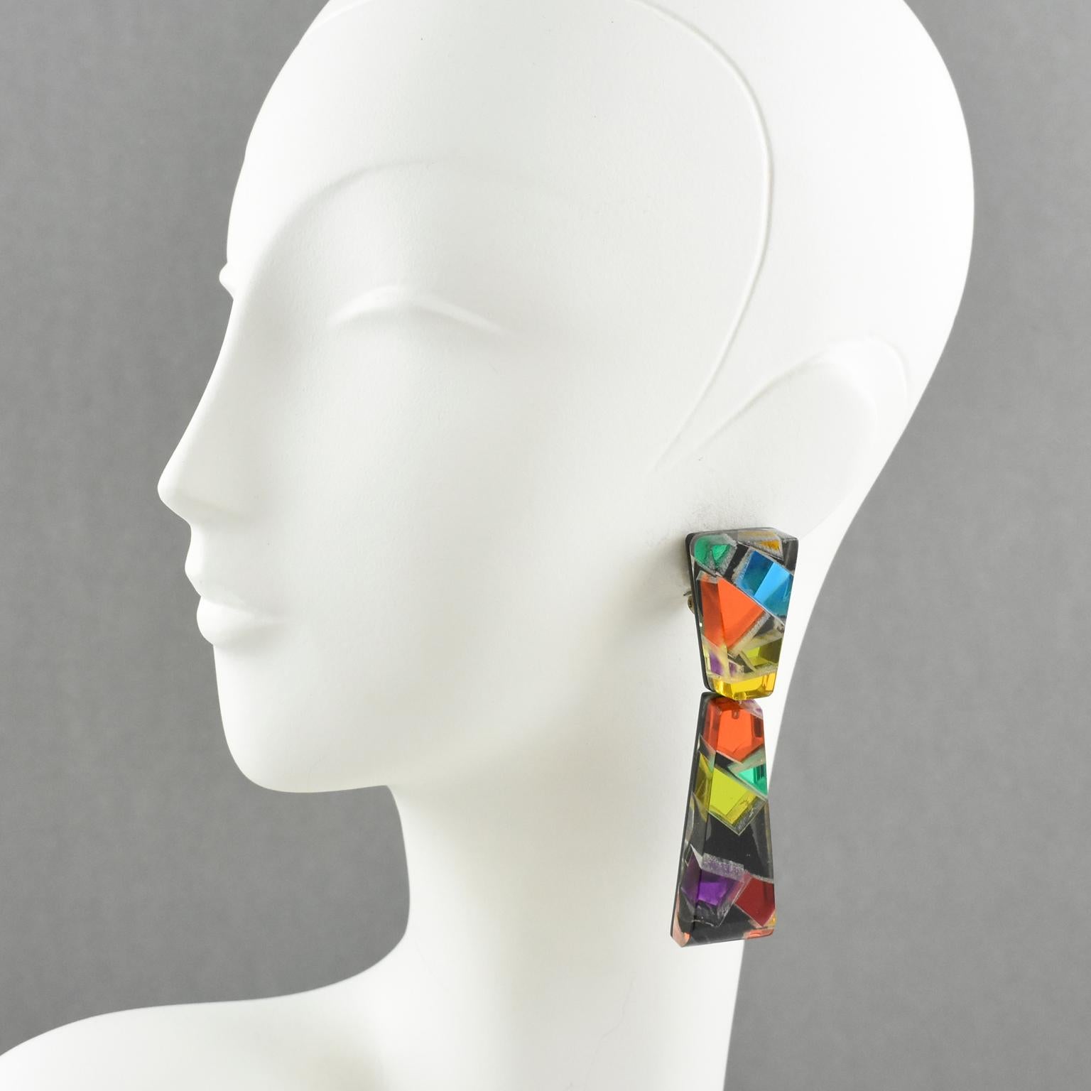 Colorful oversized Lucite chandelier clip on earrings designed by Harriet Bauknight for Kaso. Large dangling shape with geometric design featuring dimensional multilayer black lucite with colorful harlequin mirrored effect inclusions. Assorted