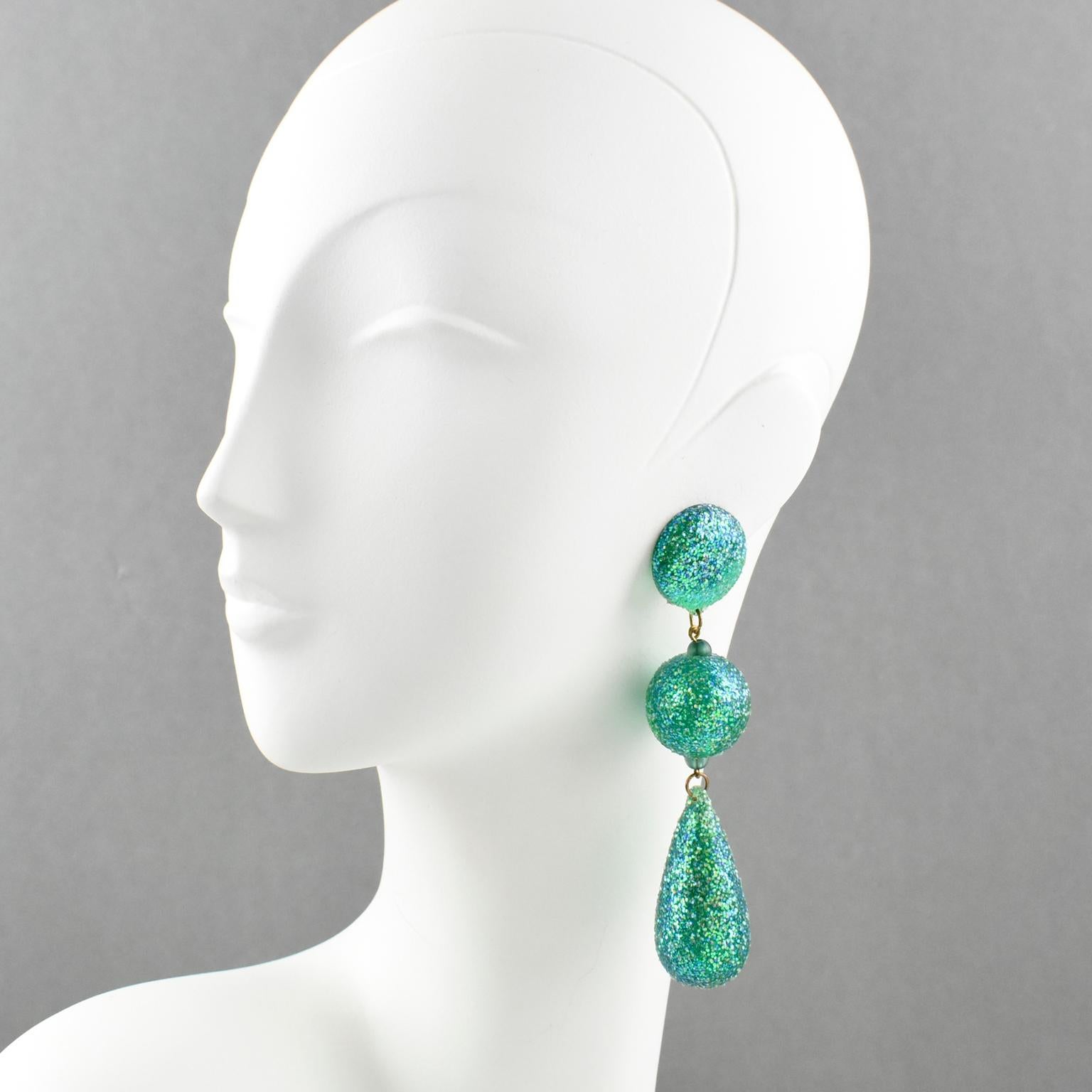 Feel like a dancing disco girl !!!
These clip on earrings are the perfect 1980s look. Oversized chandelier dangle shape with ball and drop elements in turquoise green Lucite all covered with high glitter flakes. No visible marking.
Measurements: 1