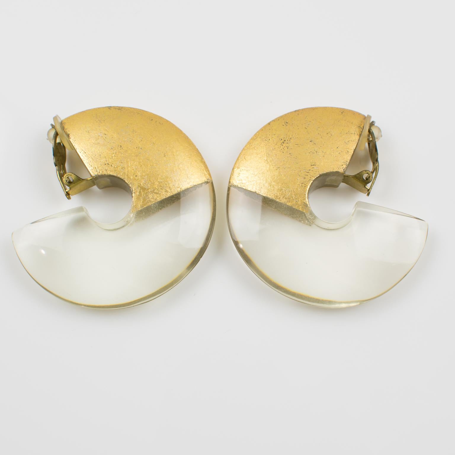Stunning oversized clip on earrings by Gerda Lyngaard for Monies. Crystal clear Lucite and gold foil application. Marked 'Monies' on clasp. 
Measurements: 2.07 in. diameter (5.2 cm) x 0.38 in. thick (1 cm)