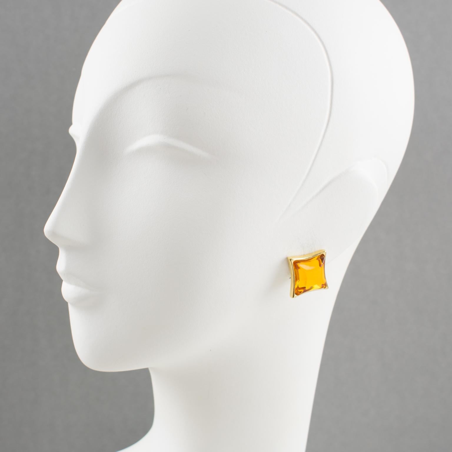Elegant Yves Saint Laurent YSL Paris signed clip on earrings. Modernist square shape, shiny gilt metal frame topped with domed poured glass cabochon in translucent honey color. Signed at the back with YSL pierced logo on clip and engraved underside: