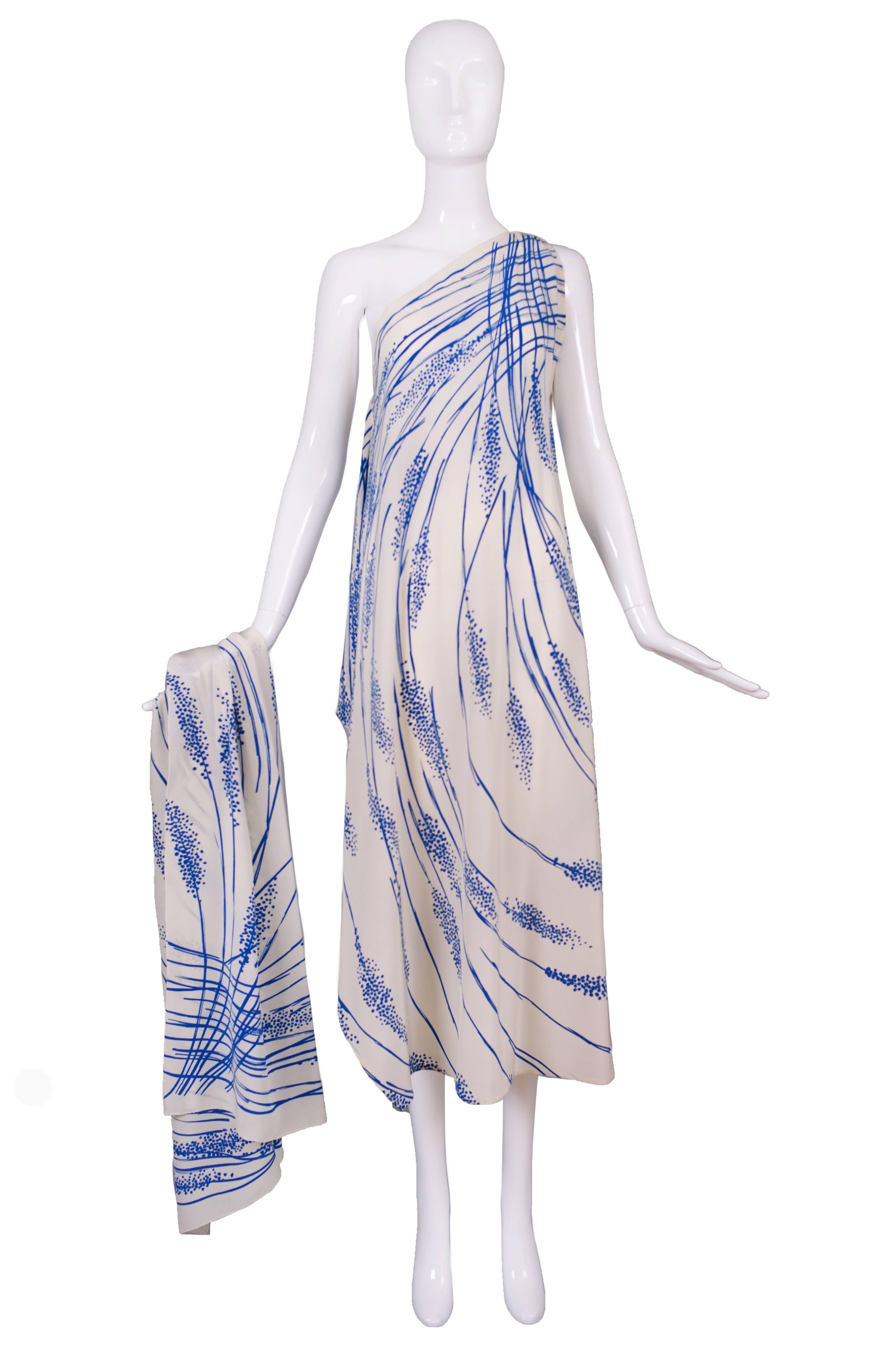 A 1970's Pauline Trigere single shoulder blue abstract grasses on cream gown with side zipper and matching rectangular wrap. There is no size tag but will likely fit a multitude of sizes. Dress is in excellent condition, some small spots on the the