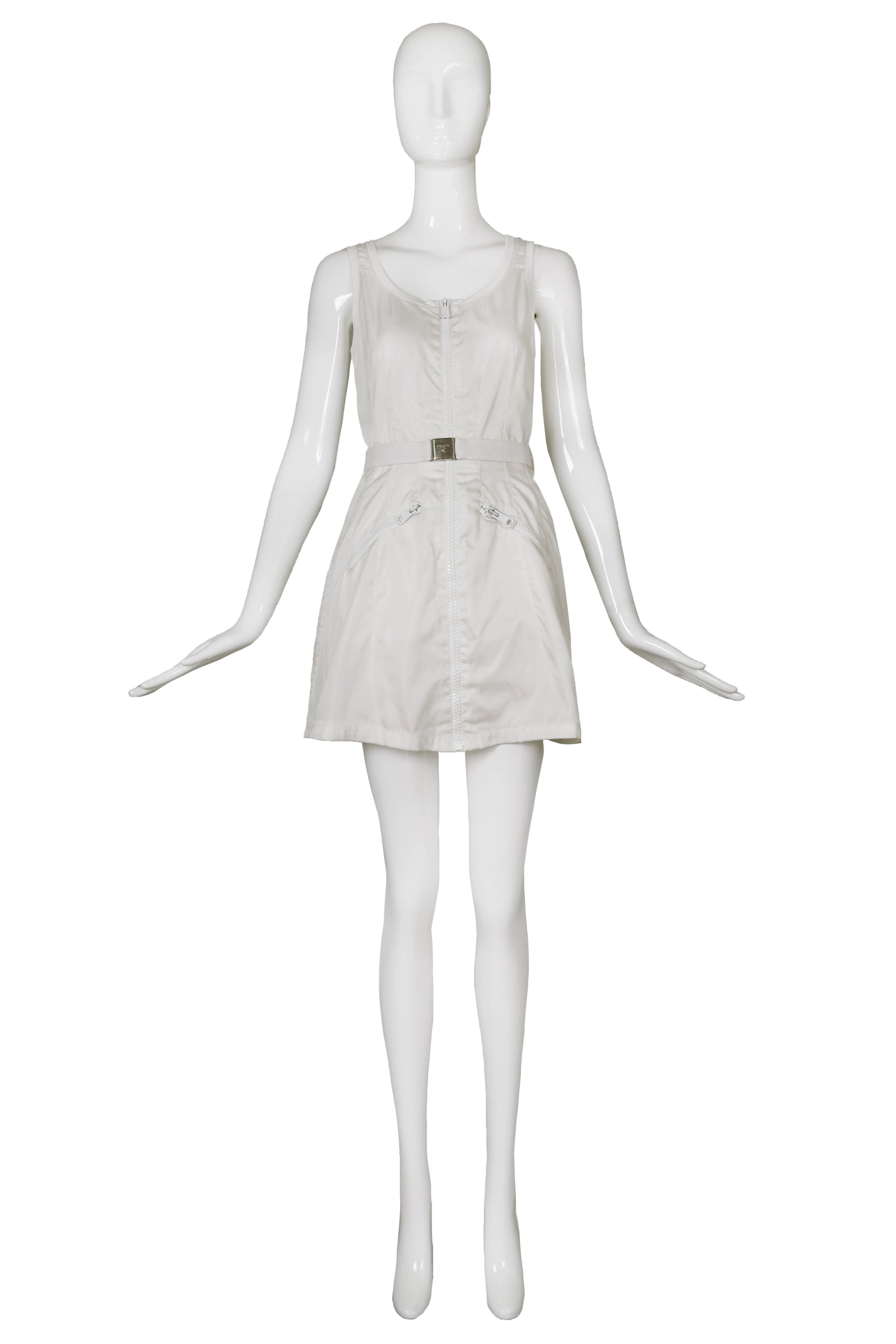Prada white mini dress with white zipper closure up center front, angled white zippered frontal pockets and elastic belt with metal Prada logo buckle. In very good to excellent condition with almost imperceptible, faded water mark at the back. Size
