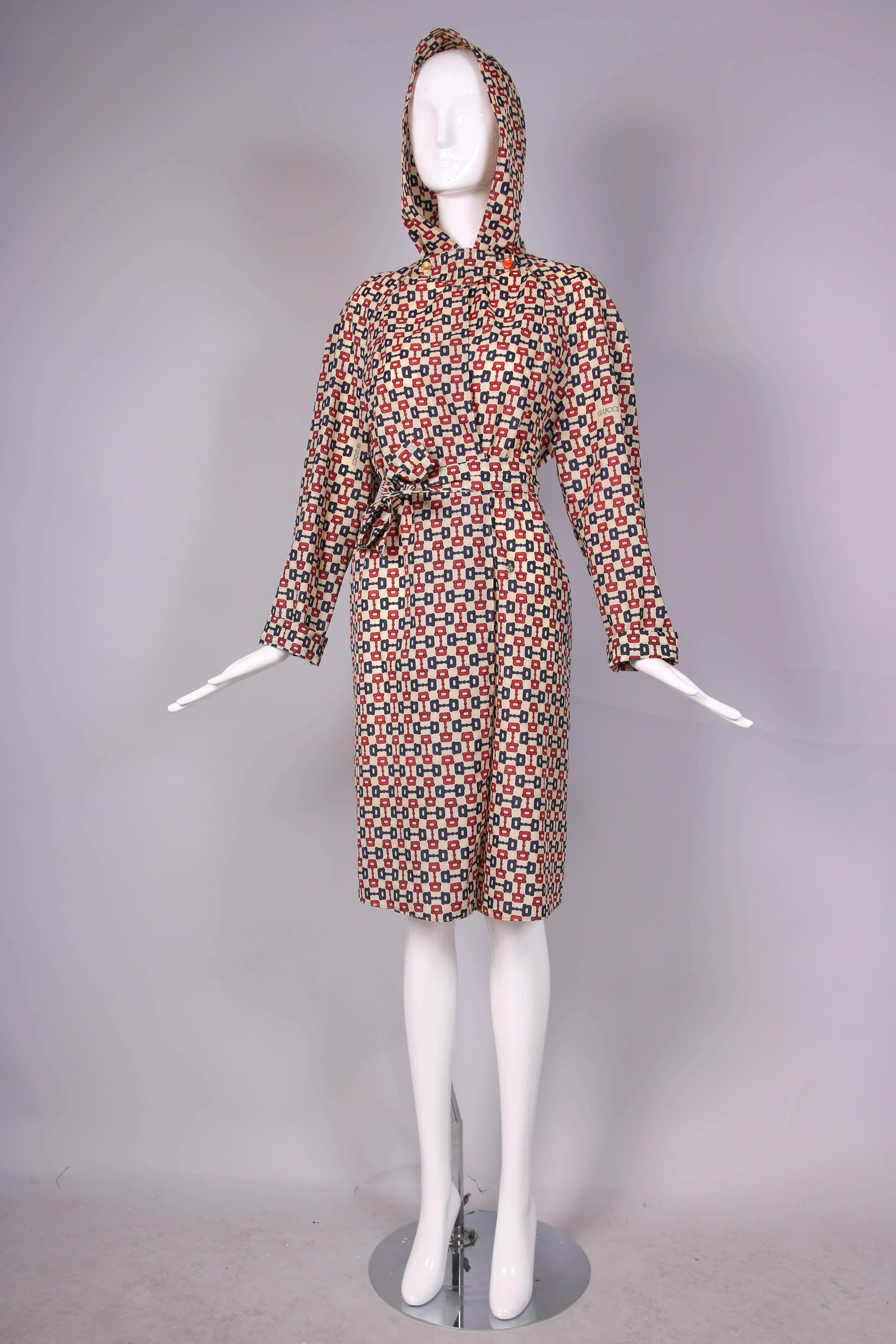 1970's Gucci iconic horsebit print hooded raincoat w/belt. Gucci logo included in print in three places. Snap closure. Two glazed Gucci buttons at neck - one button is missing glaze. Comes with pouch - raincoat folds up and fits inside - perfect for
