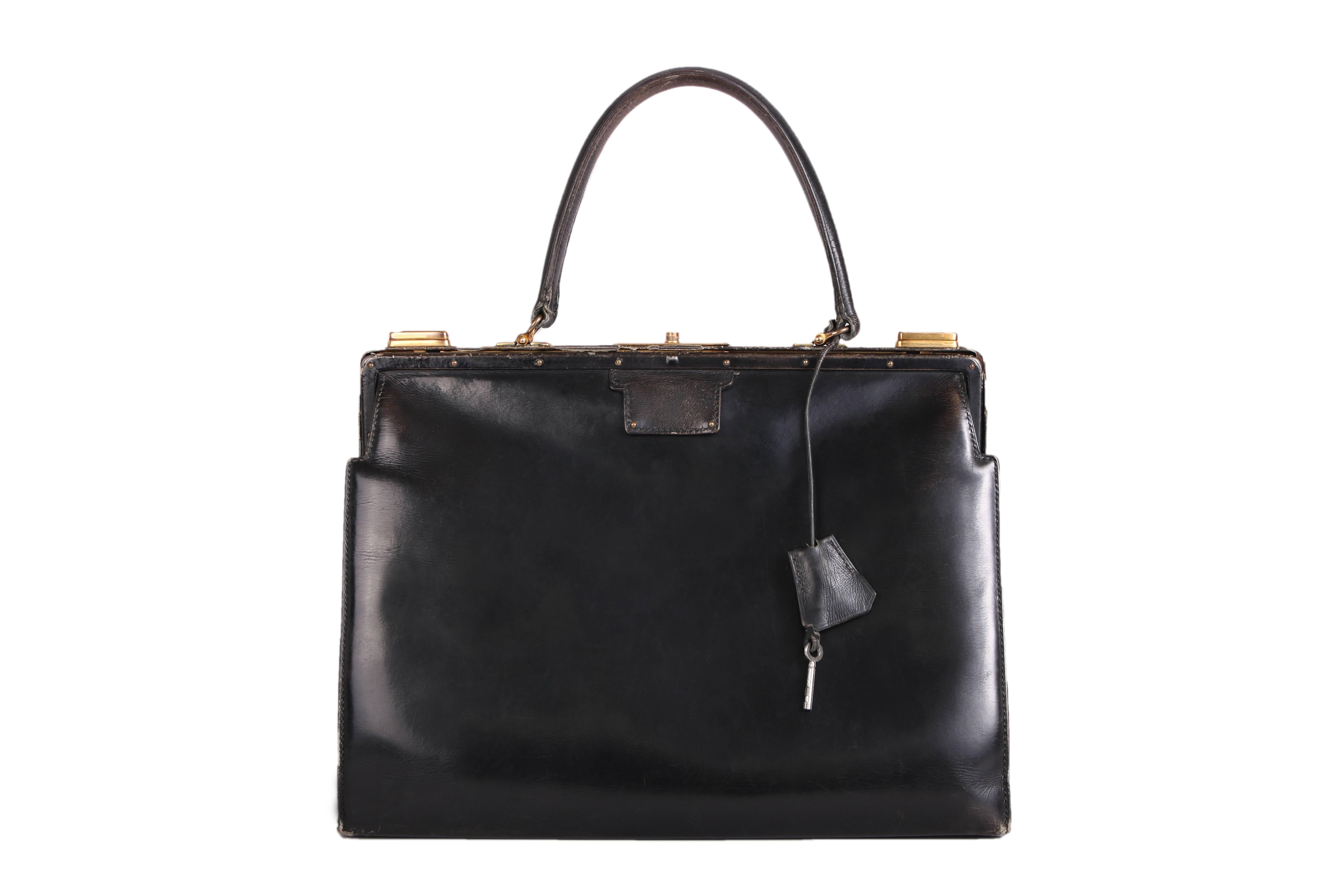 Vintage Hermes black leather handbag with lock & key. Features gold hardware and black leather interior. In good vintage condition with minor scratches and scuffs at the interior and exterior. There is some peeling of the leather covering the metal