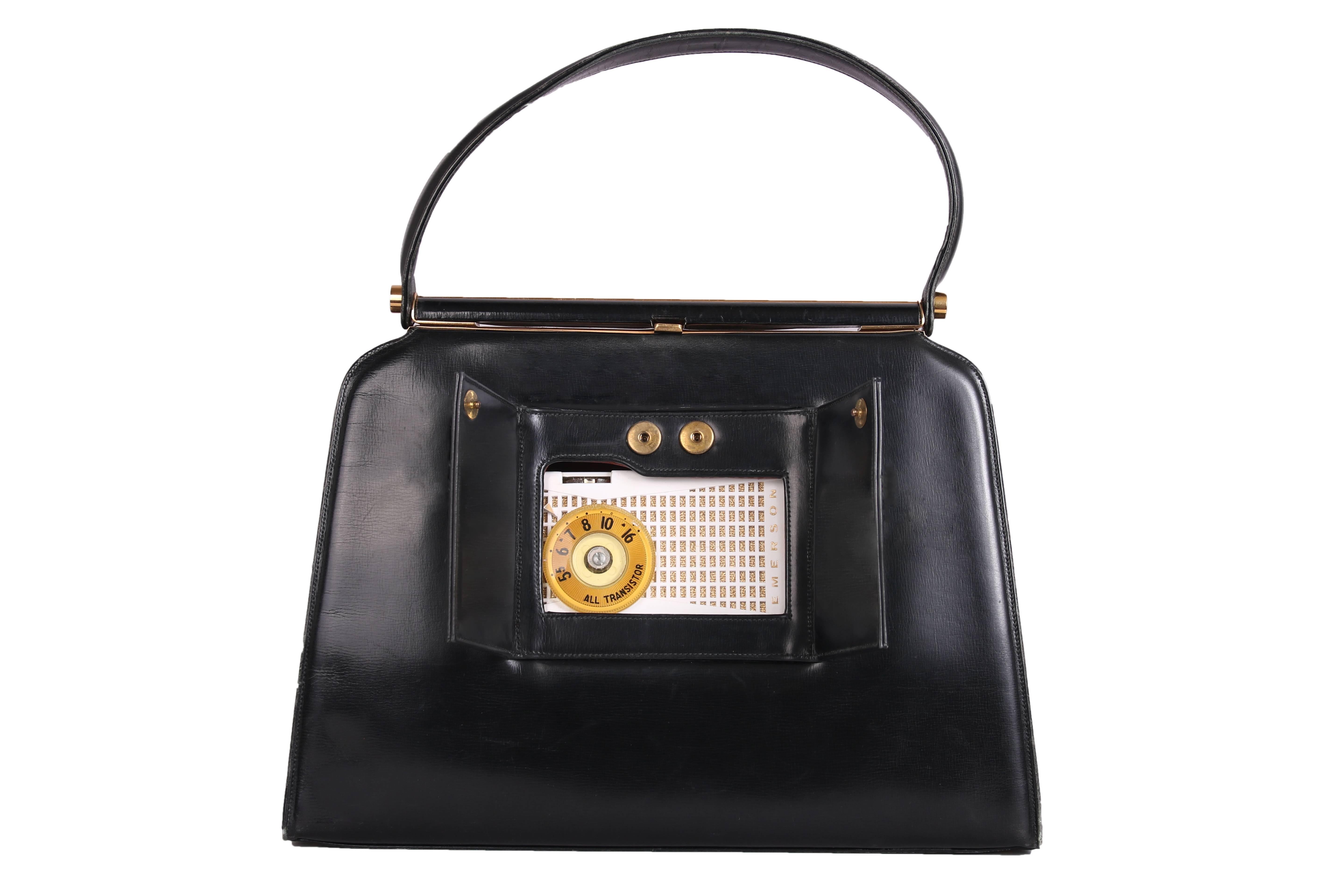 1960's Frank Milch black leather handbag with two frontal snap closure flaps that reveal a working radio. Features a clasp closure, gold hardware and brown leather interior with three interior storage pockets. In good vintage condition with minor