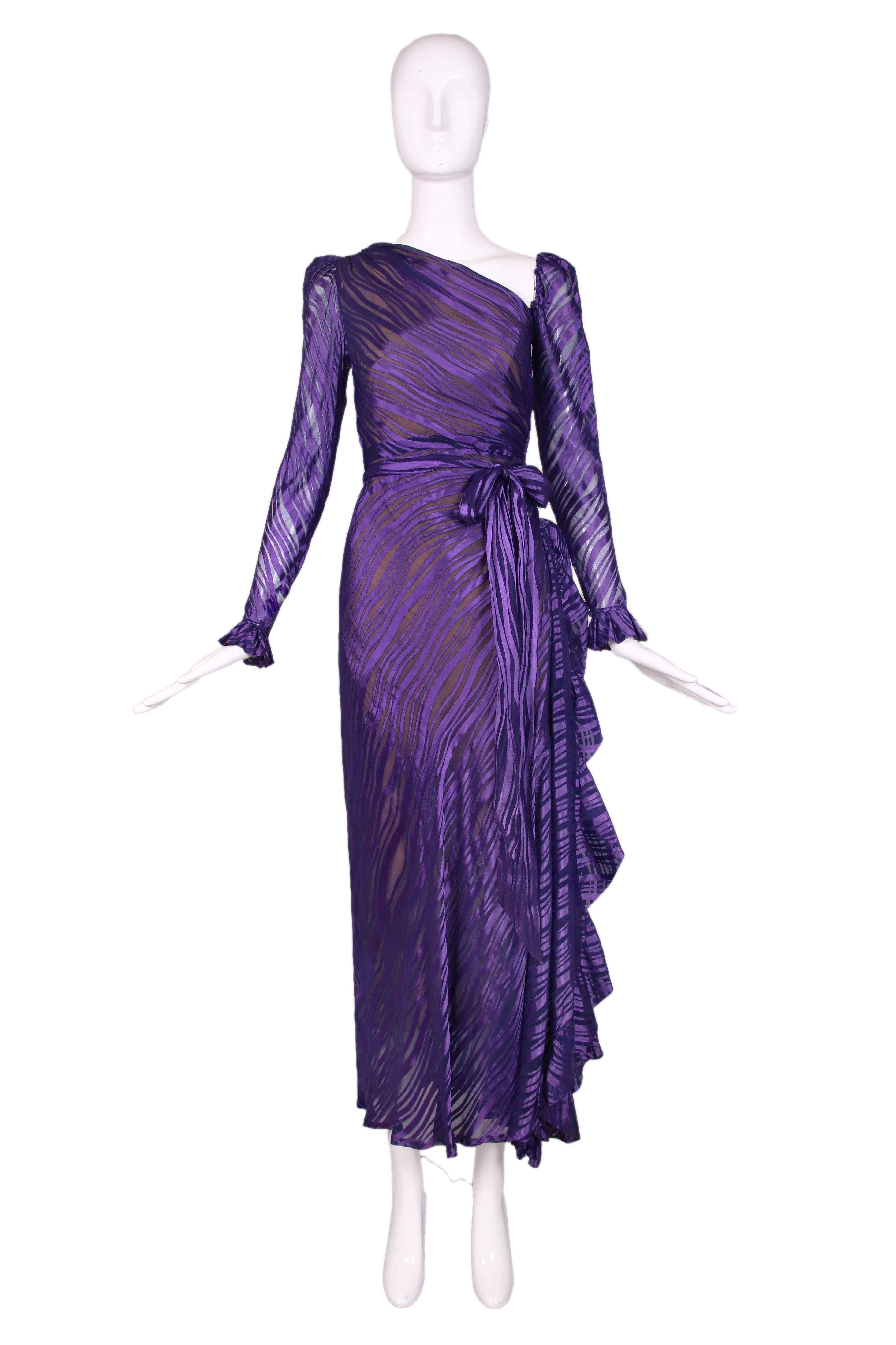 1970's Yves Saint Laurent sheer silk damask gown in deep royal purple. The dress has an asymmetrical neckline, classic YSL ruffles at the cuffs and side slit with a self sash belt. This dress is a show stopper. In good vintage condition with tiny