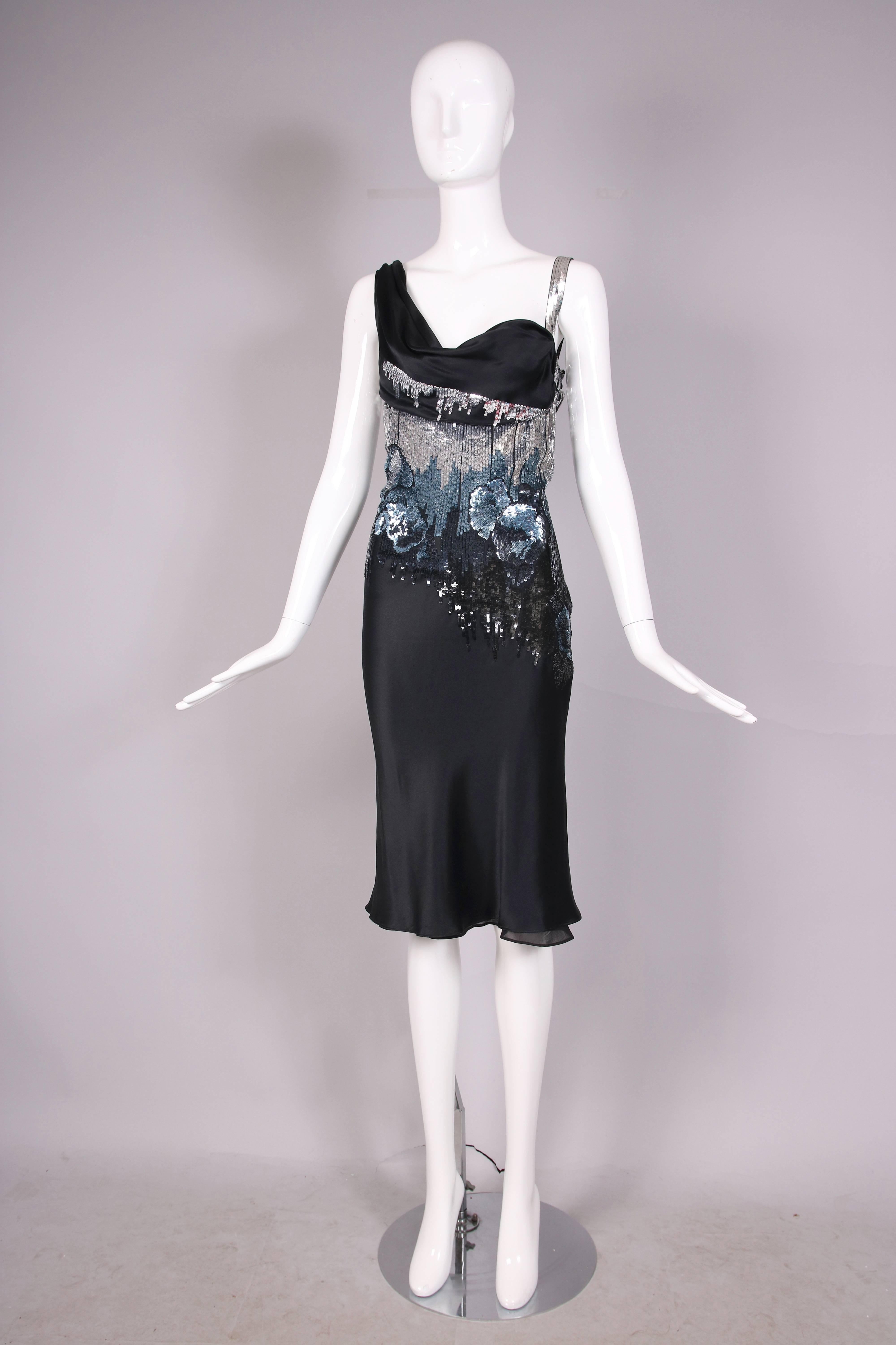 John Galliano black silk charmeuse cocktail dress with the bodice featuring silver, blue, and black sequins in a graphic ombre print as well as sequined roses. One should strap is made entirely of silver sequins and the bust is draped with black