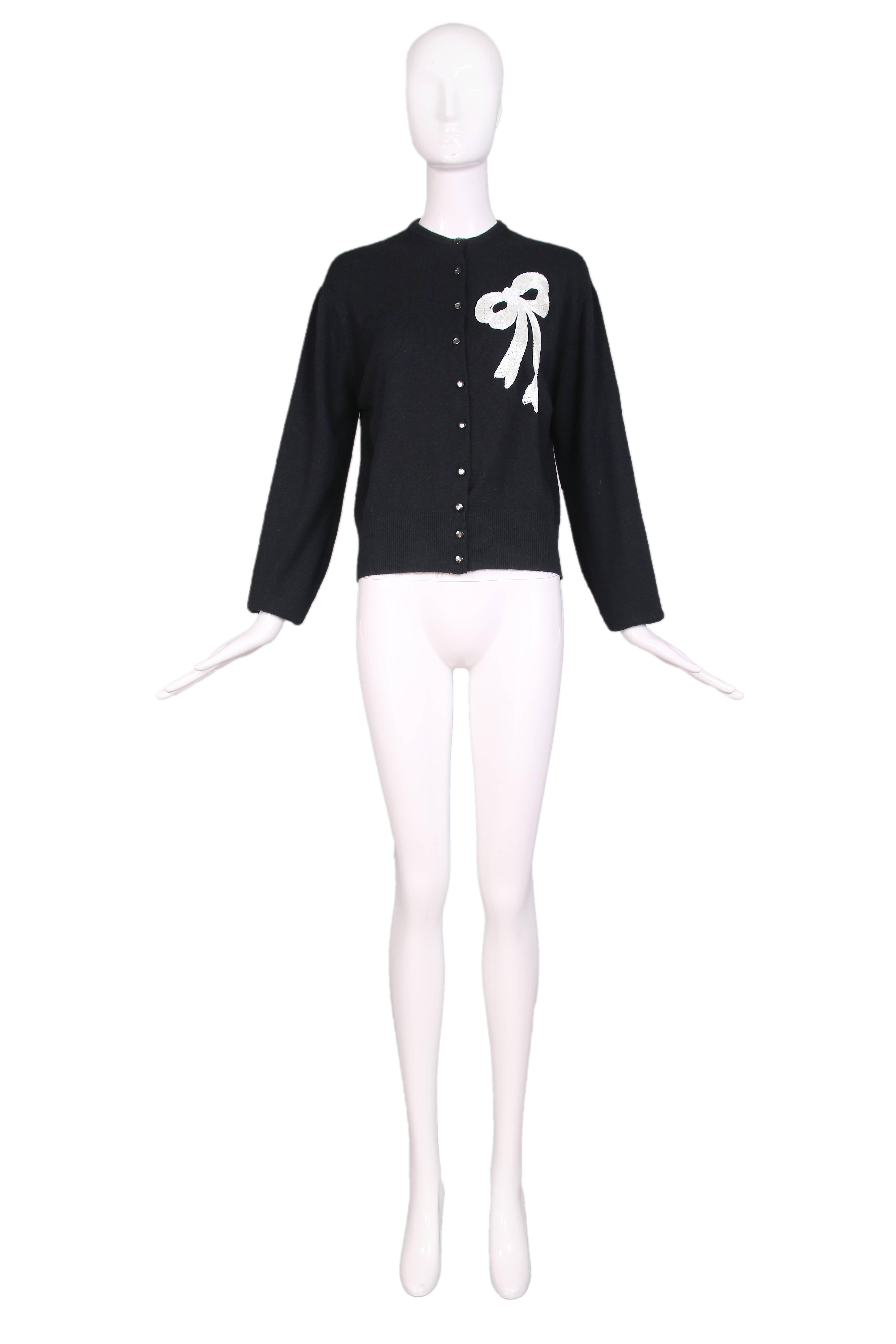 Vintage Schiaparelli black cashmere long sleeved cardigan sweater with pearlized black buttons down the front and silver beading in the shape of a bow embroidered on left front. In excellent condition. 
MEASUREMENTS (in inches):
Bust - 42
Waist -